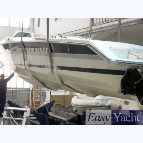 A large white motorboat inside a warehouse, elevated on stands, with a smaller inflatable boat beneath it. The warehouse has metal beams and windows, and a man is standing nearby.