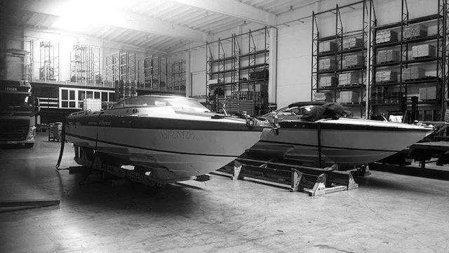 Two boats inside a warehouse or workshop, surrounded by shelves with boat parts and equipment.