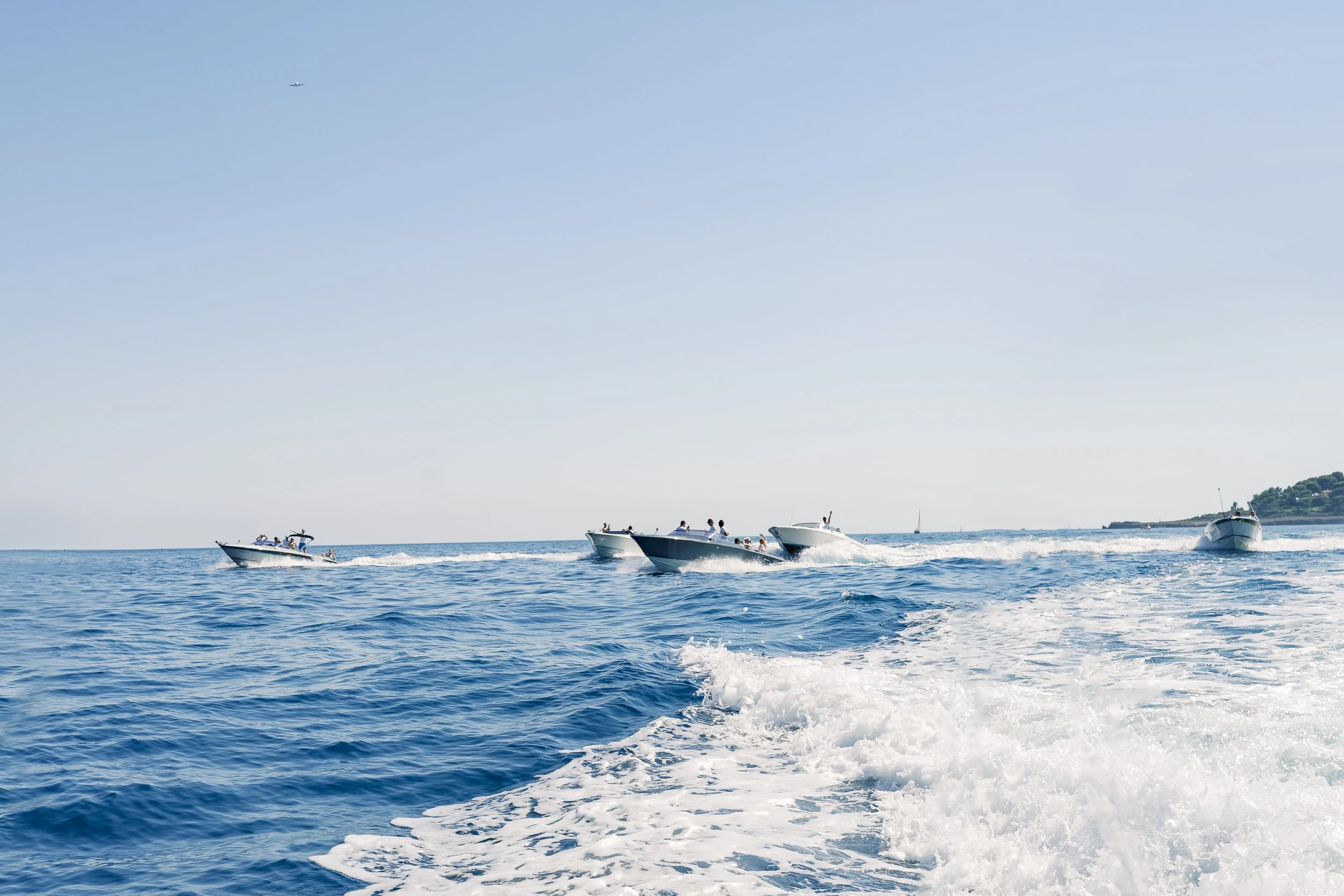 Several boats speeding across the ocean, creating waves and leaving white foamy wakes behind them, with a clear sky above.