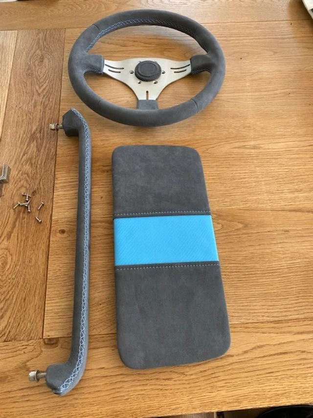 Disassembled gaming steering wheel with base, metal bar, and padded cushion on a wooden surface