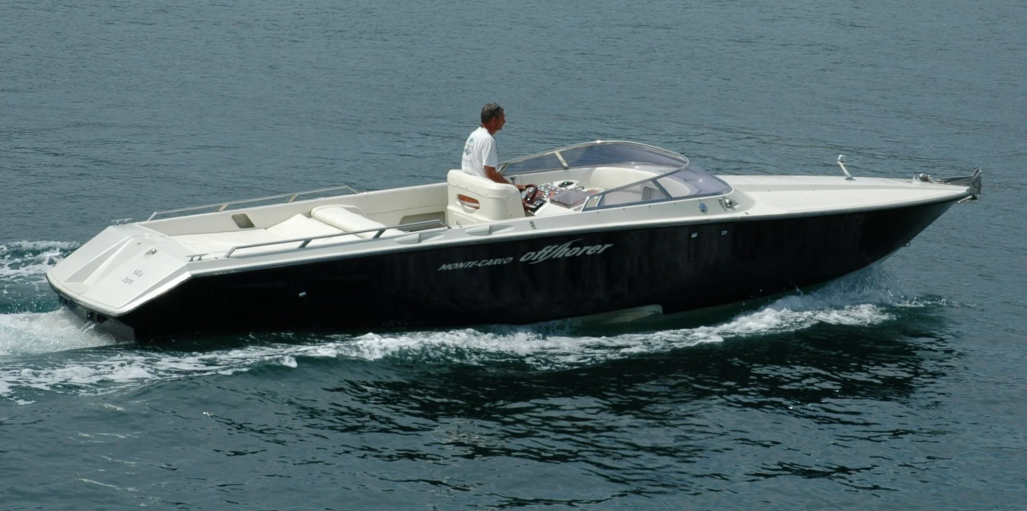A man driving a sleek black and white motorboat on open water.