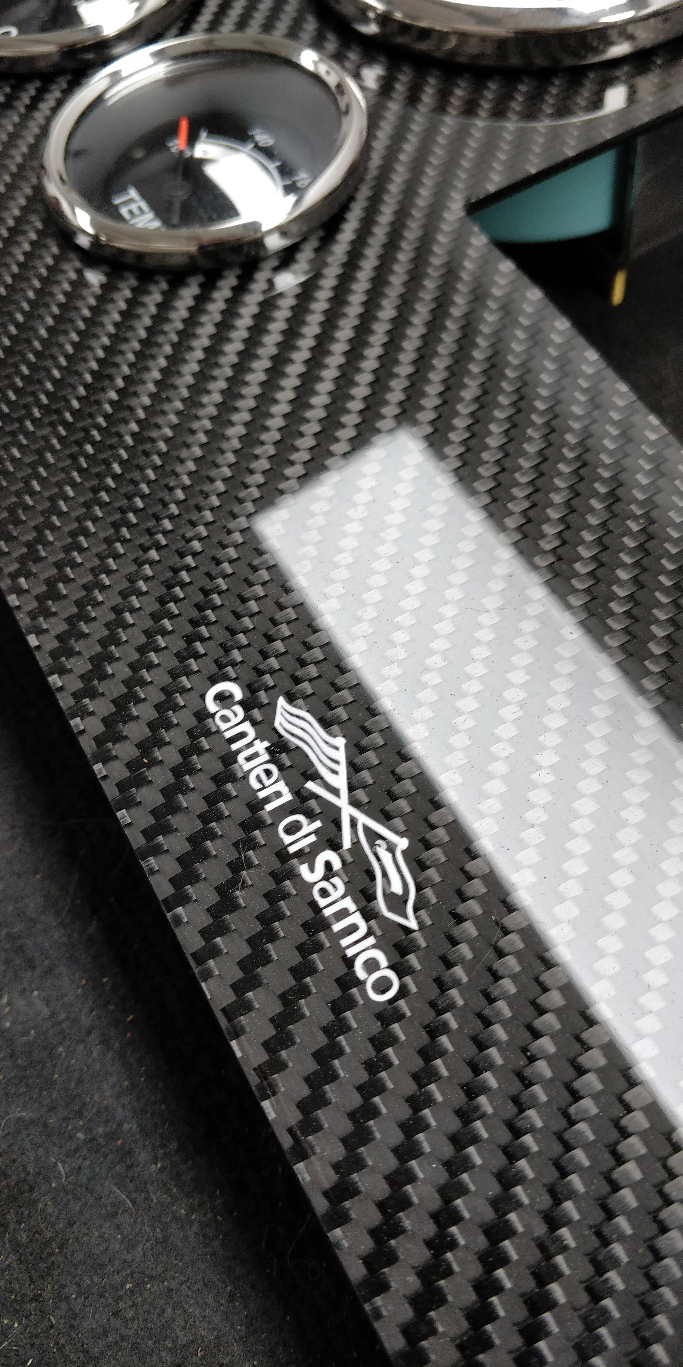 Close-up of a carbon fiber panel with a tire pressure gauge and a logo that reads 'Center Sanico' and includes a stylized sailboat icon.