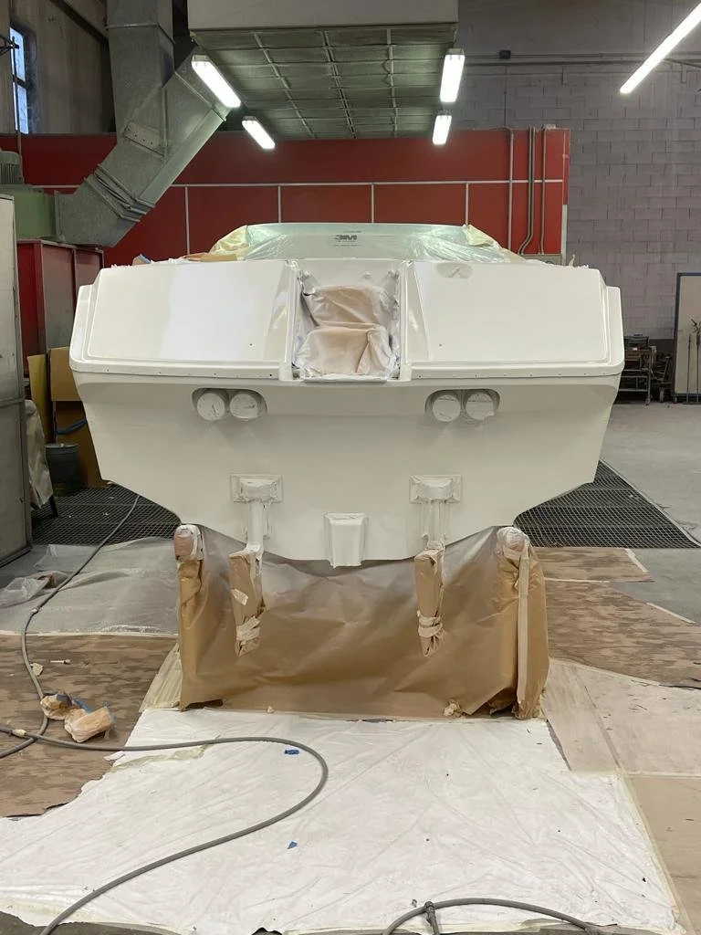 A boat under construction in a workshop, with wrapped sections and a partially painted white hull, surrounded by tools and protective coverings.