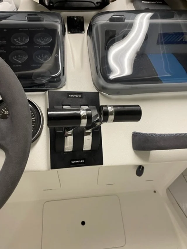 View of a boat's control panel with a steering wheel, a throttle or gear shift, and clear protective covers over instruments and electronics.