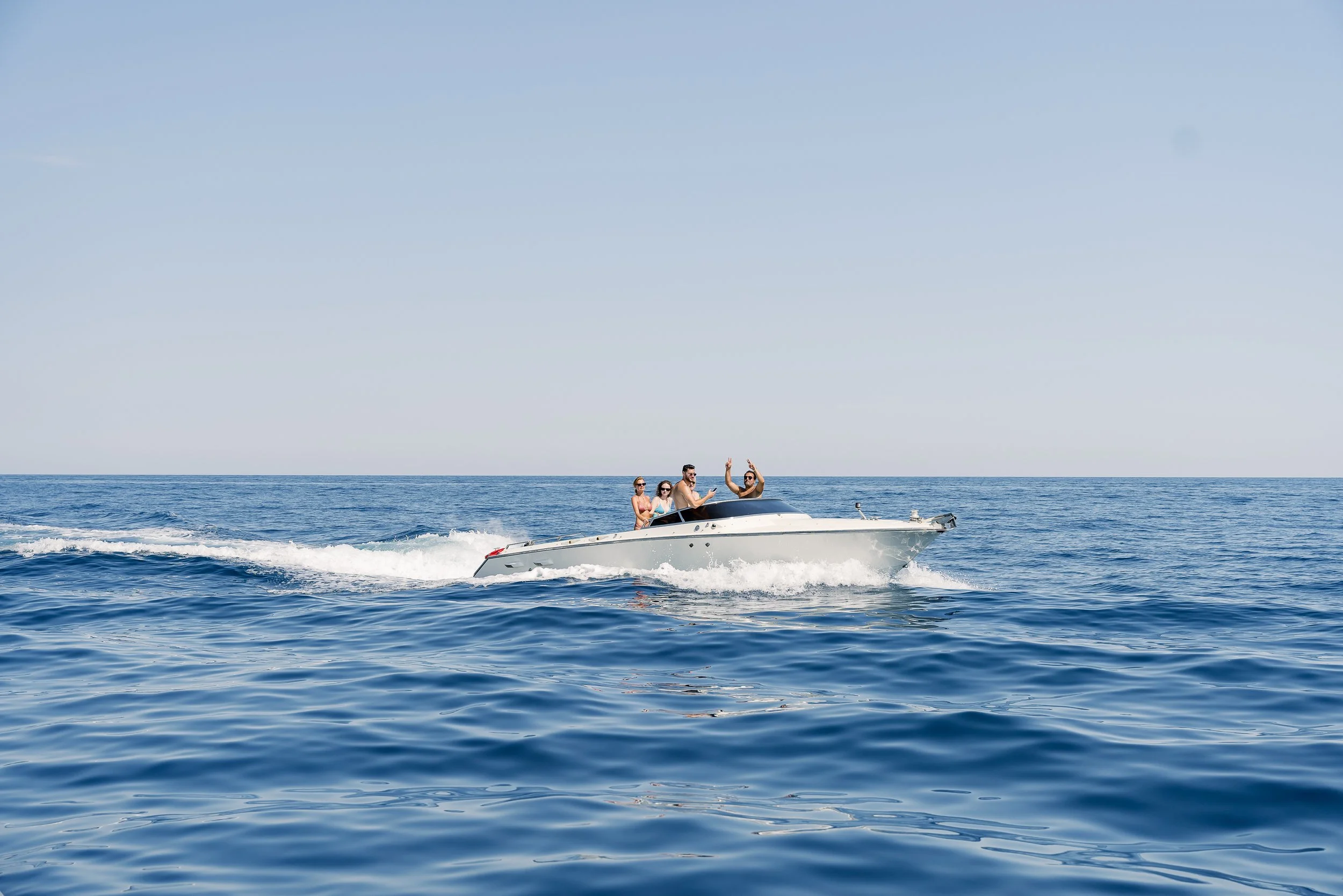 A group of five people enjoying a boat ride on the open ocean, with clear blue water and a light blue sky.