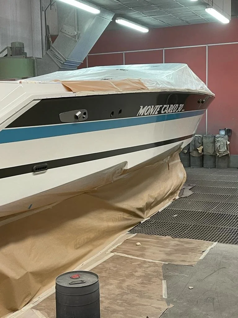A boat in a workshop, partially covered with brown paper and plastic, with painting or maintenance materials nearby.