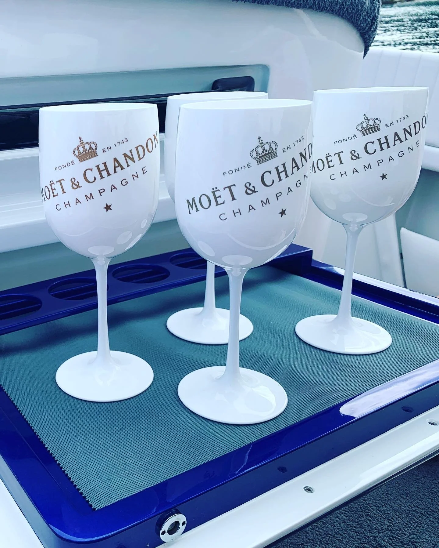 Four white Moët & Chandon champagne glasses on a green surface with a blue border, with the logo and text printed on each glass.