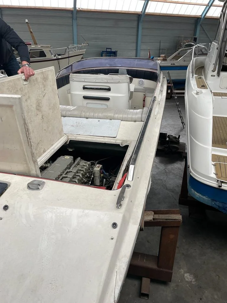 A boat in a warehouse, with a person working on it, surrounded by other boats and boat equipment.