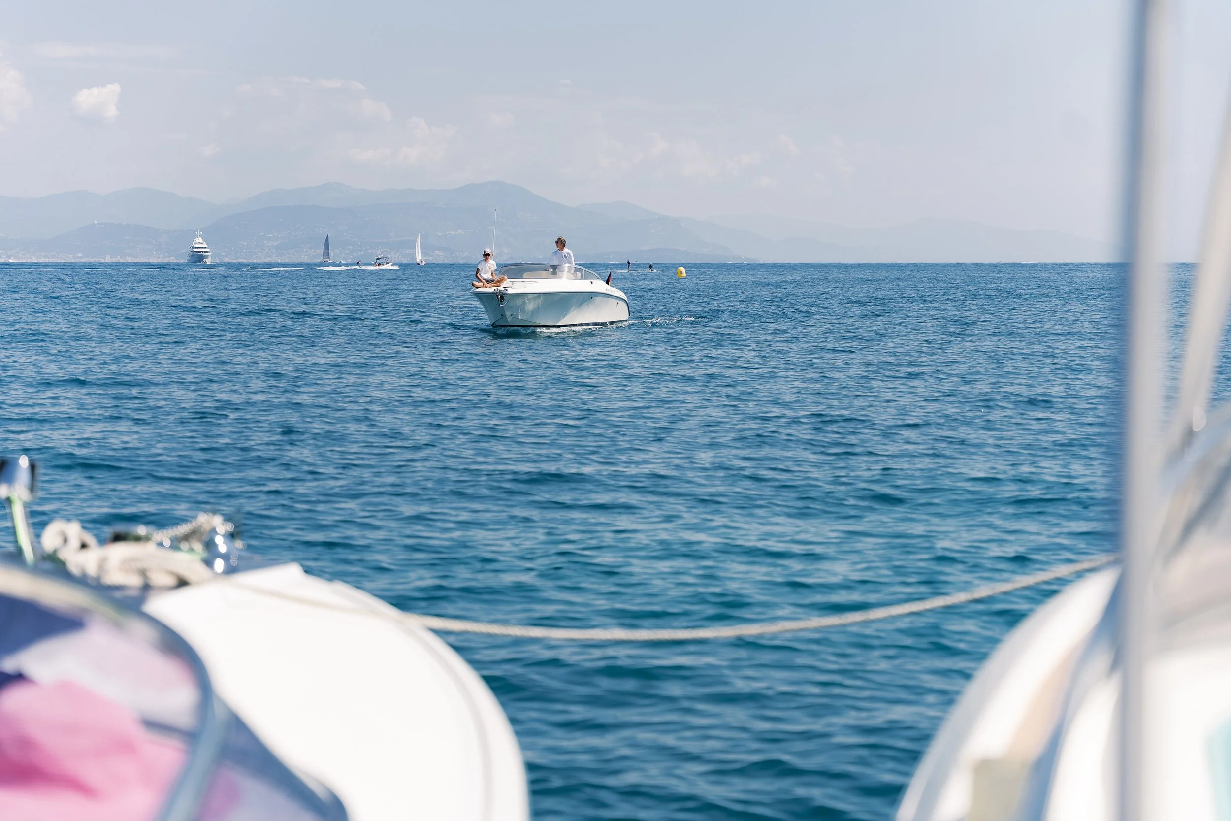 Boat on the water with mountains and cloudy sky in the background, viewed from another boat's deck.