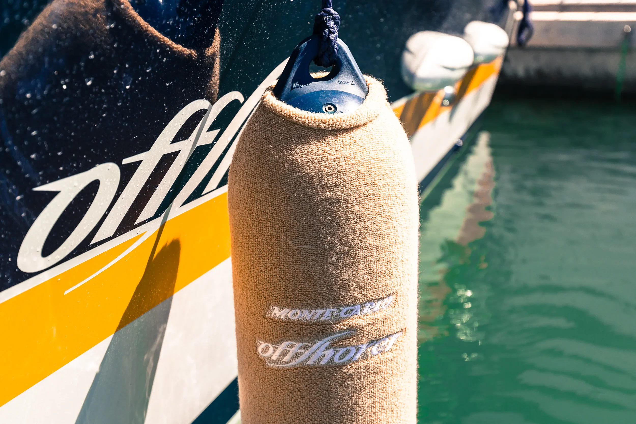 A beige towel labeled 'Move Gear offshore' draped over a fender attached to a boat with a visible part of the boat and water in the background.
