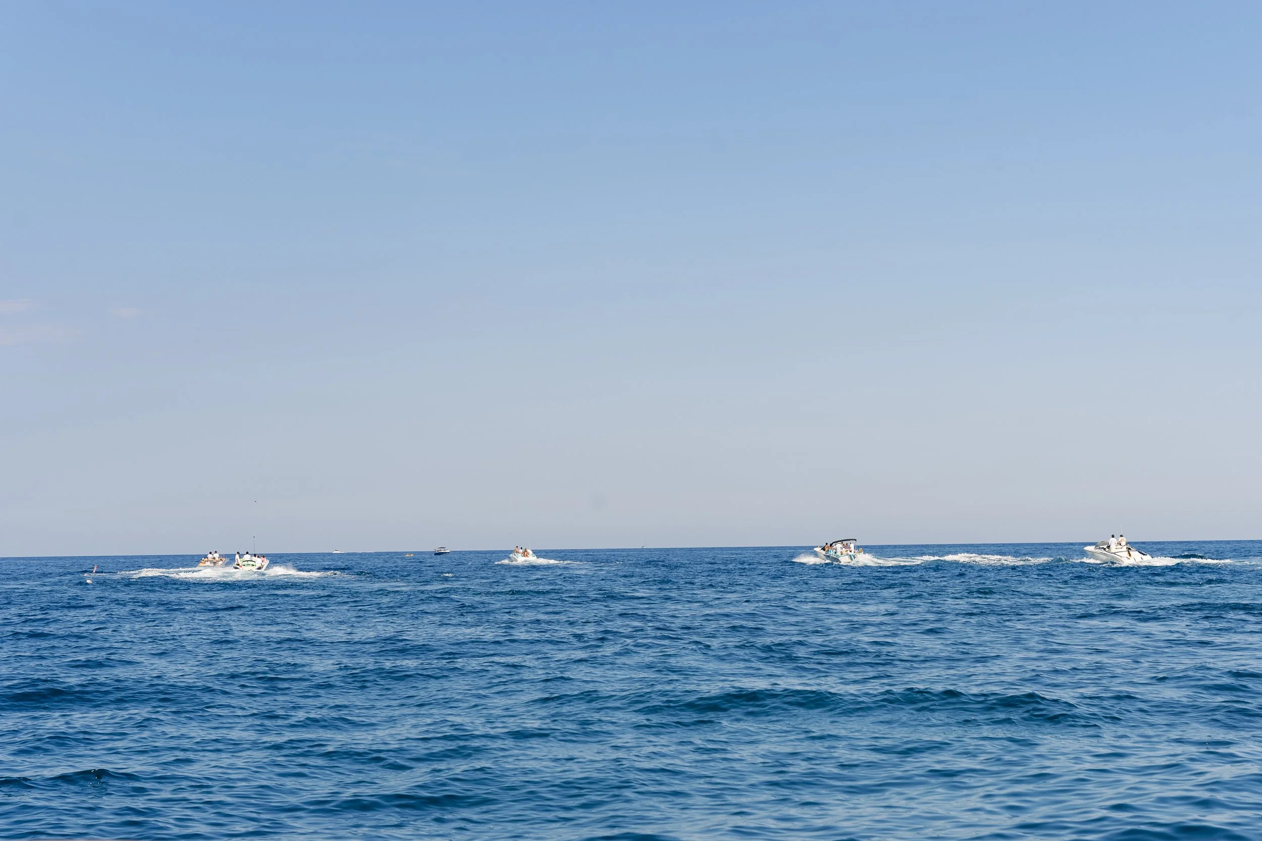 Multiple boats on the open ocean under a clear blue sky.