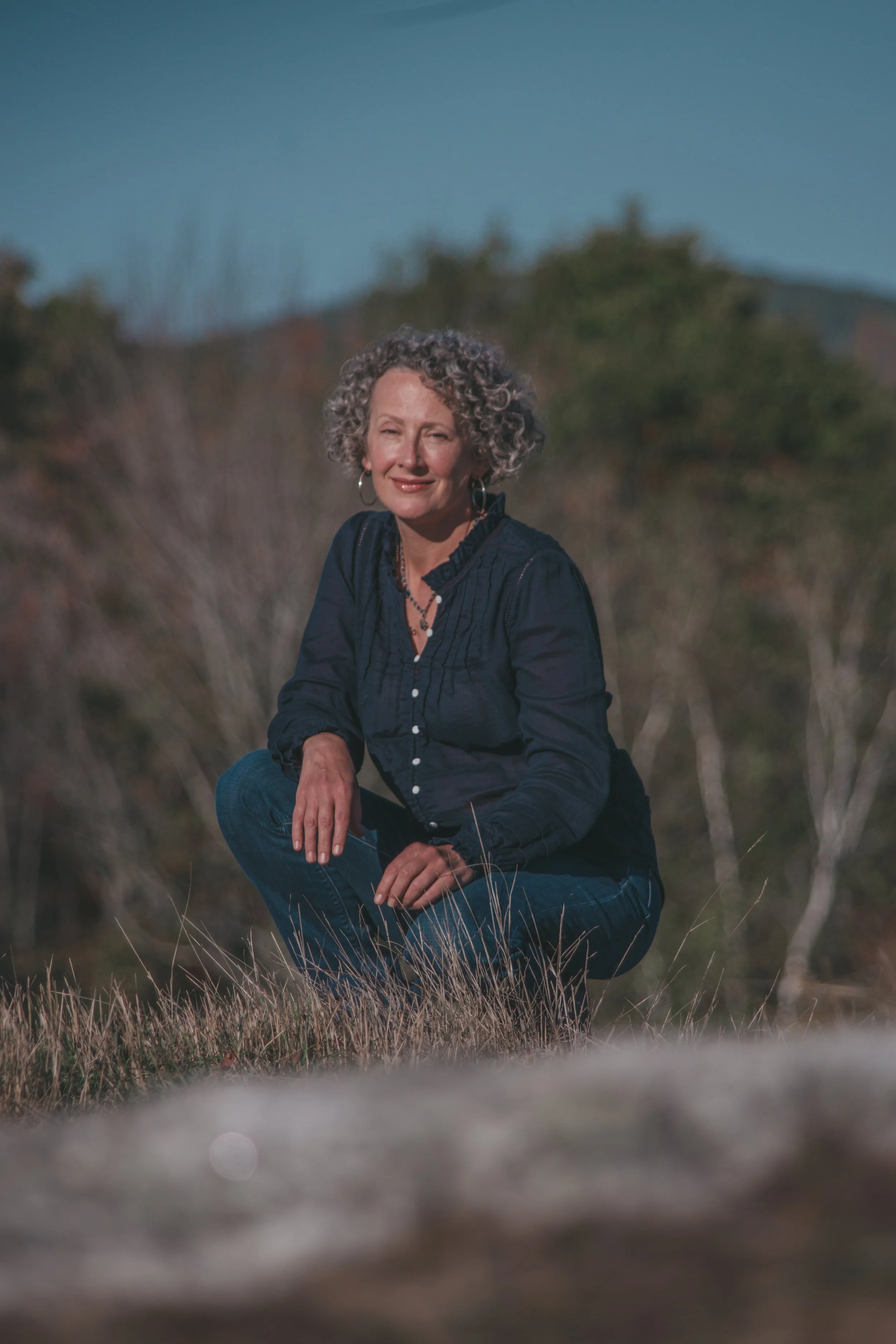 Dressed in a navy blouse with silver hoops in her ears, Kimberly smiles enigmatically while seated in a late autumn field