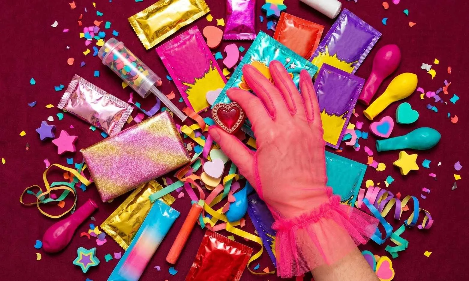 Pink tulle-gloved hand sorting through colourful celebratory objects, illustrating how positive emotional arousal increases impulse buying behaviour