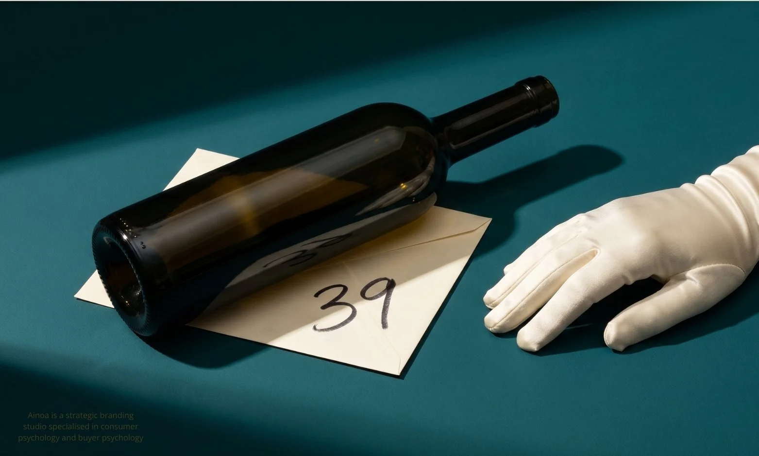 A wine bottle beside a handwritten price tag and an ivory-gloved hand on a teal background — referencing the MIT anchoring study by Ariely, Loewenstein and Prelec.