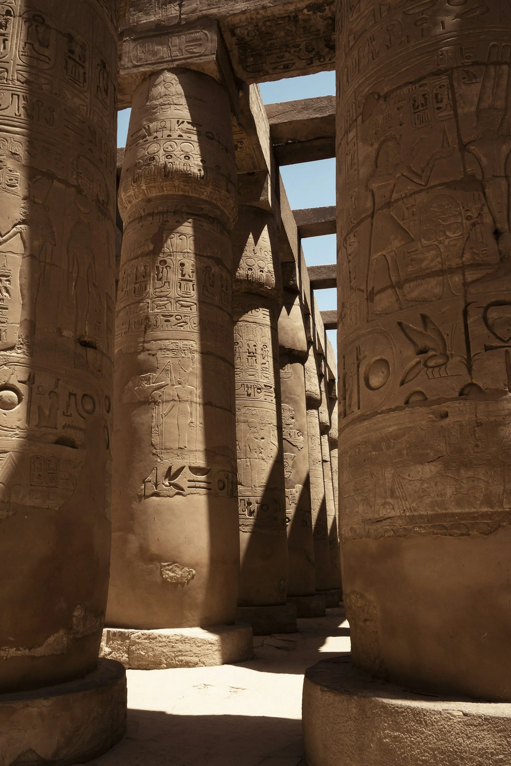 Ancient Egyptian stone temple with tall, carved columns inscribed with hieroglyphics and images of Gods, set against a clear blue sky.