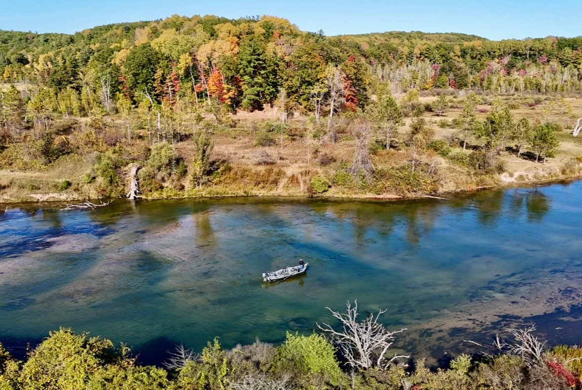 A boat floating on a river surrounded by trees with colorful fall foliage.
