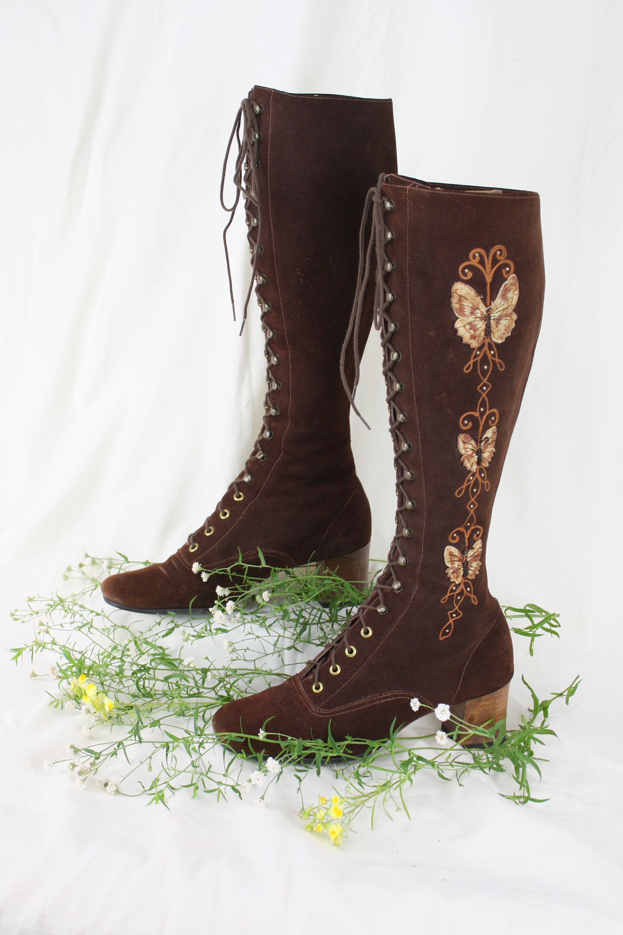 Vintage Lace Up Knee High Boots in chocolate brown suede with Butterfly Motif Embroidered Butterfly motif and gold studs on a muslin backdrop with wildflowers. Heirloom vintage accessories for sale.