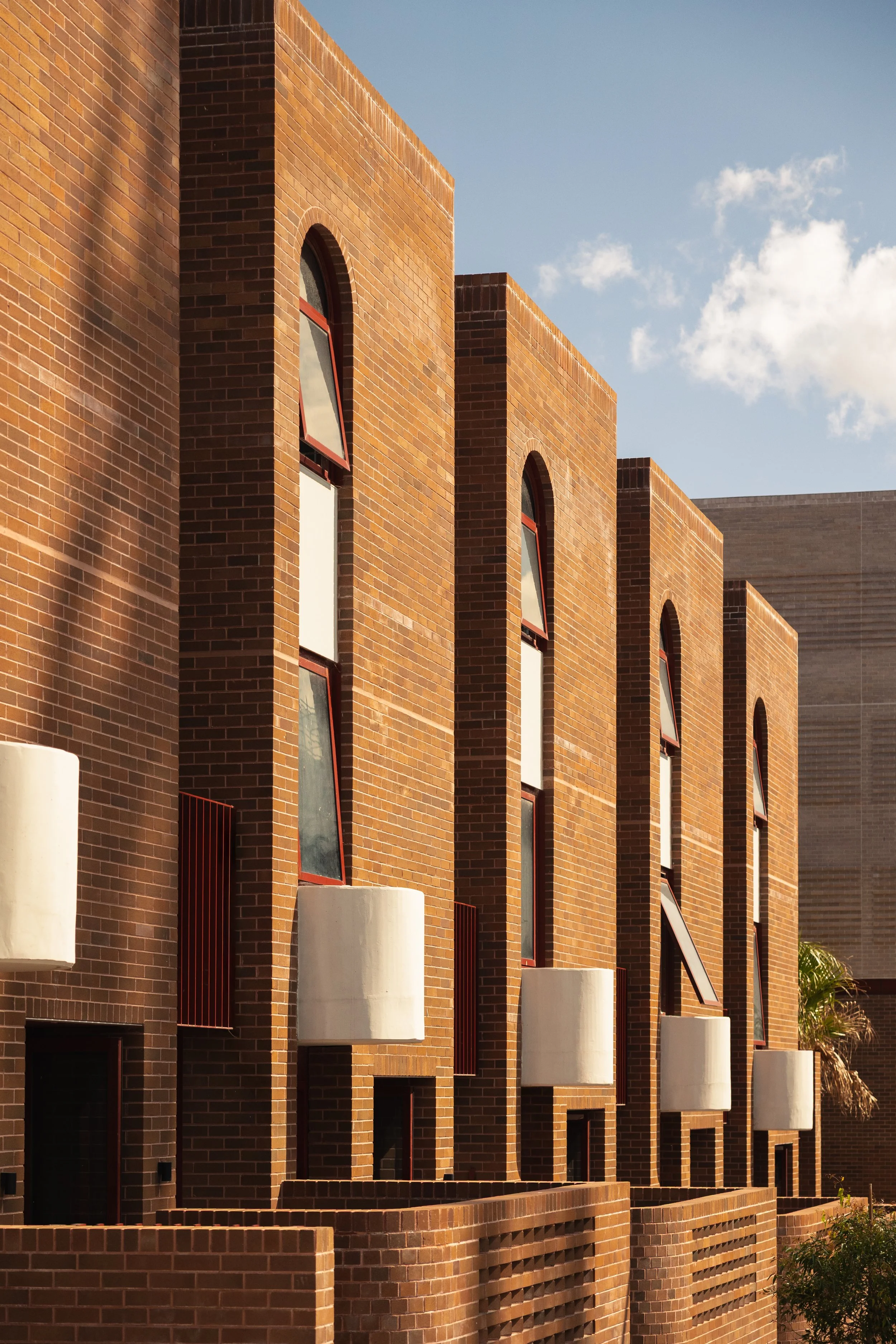 A modern brick building with multiple arched windows and white balcony planters, under a partly cloudy blue sky.  Luxury architecture design, high end residential development