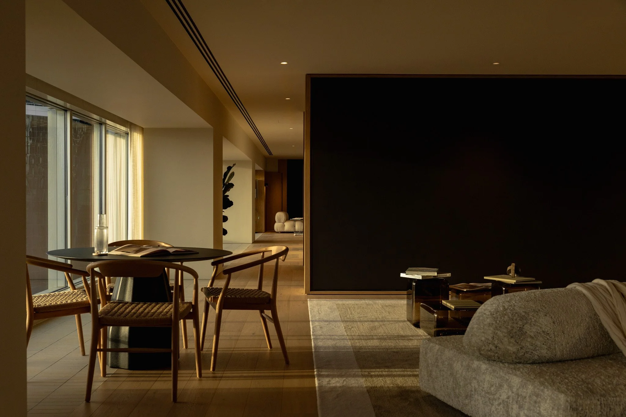 Modern living room with round dining table and chairs near large windows, a black partition wall, and a cozy seating area with books and decor.