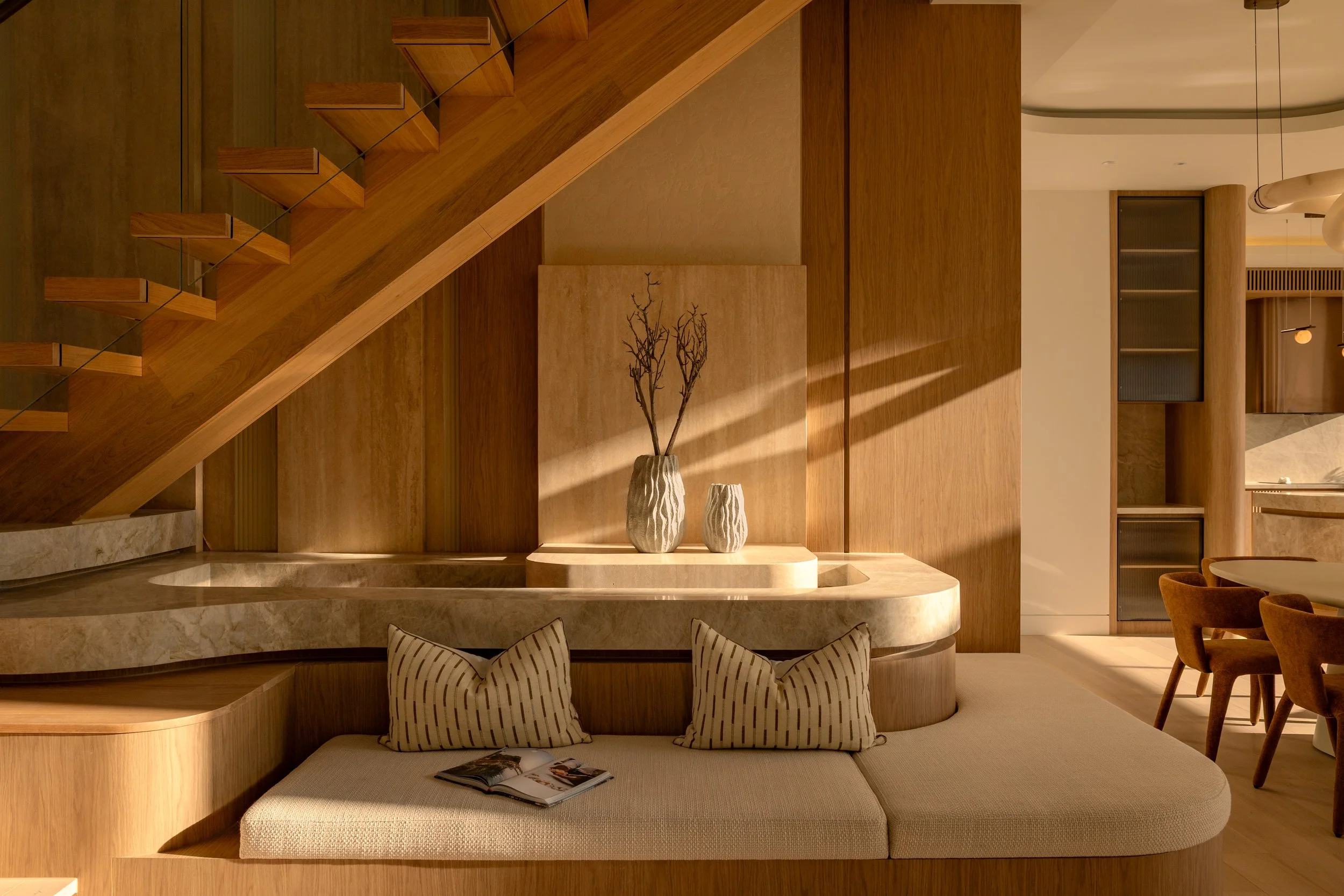 Modern interior with wooden staircase, beige curtains, and a seating area with striped pillows and an open magazine.