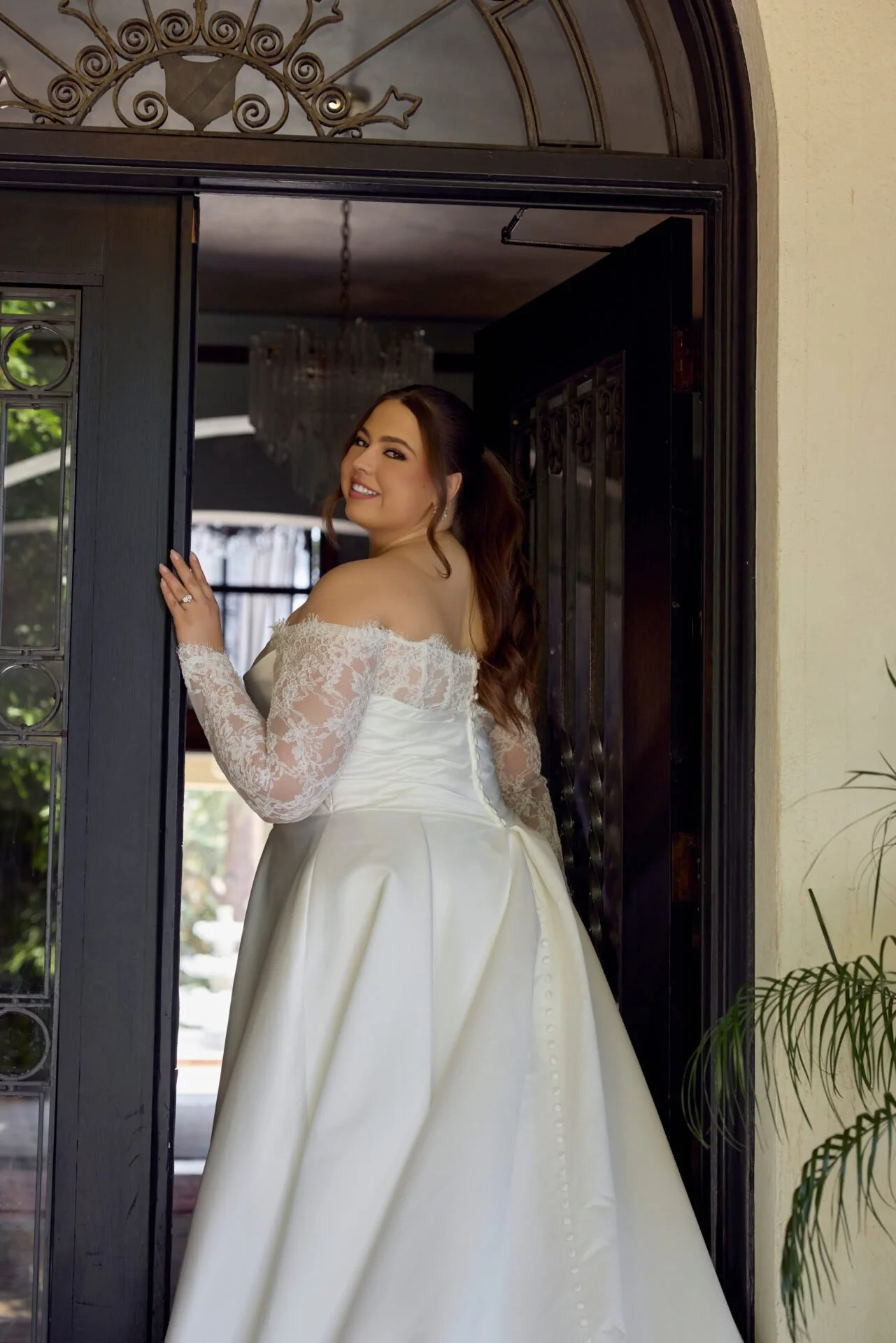 close up of back of plus size bride wearing ivory satin aline wedding dress with basque waist and lace off the shoulder long sleeves
