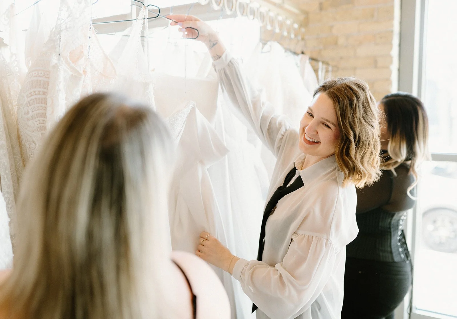 Women shopping for wedding dresses in boutique with lace gowns hanging on a rack, smiling and admiring dresses.