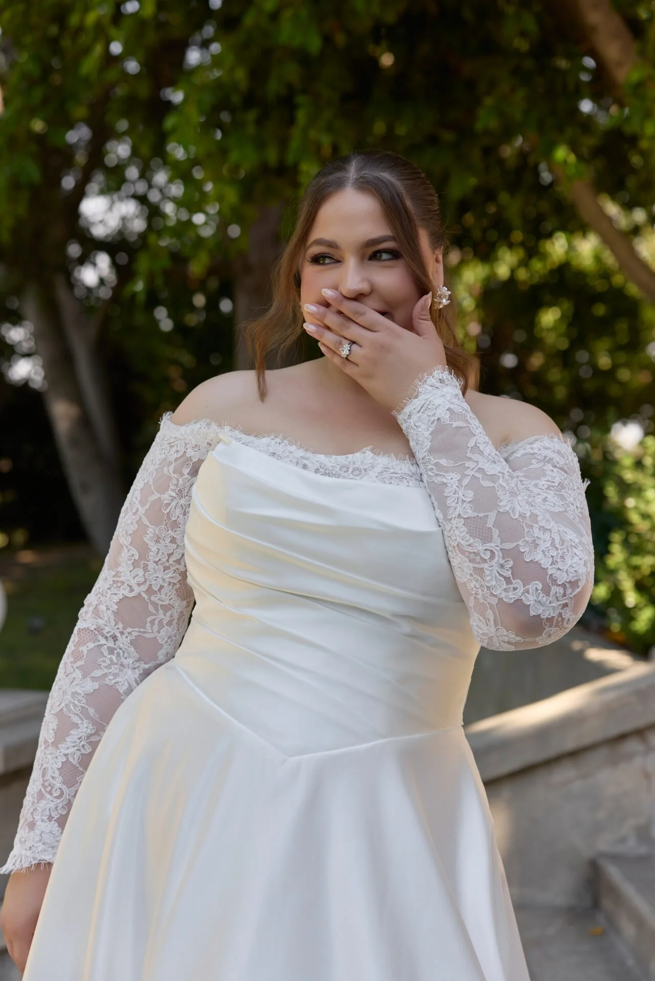 close up of plus size bride wearing ivory satin aline wedding dress with basque waist and lace off the shoulder long sleeves