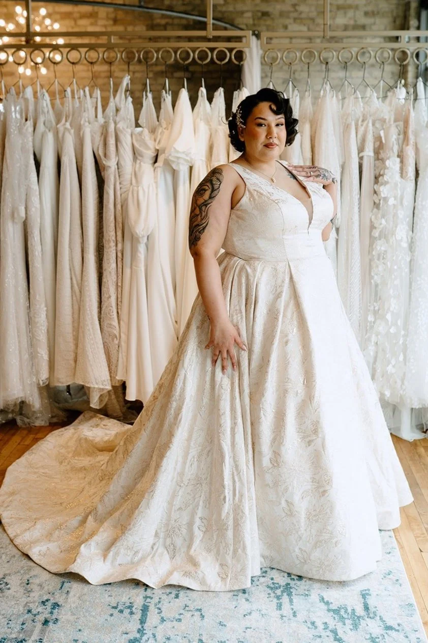 Woman trying on a wedding dress in a bridal shop surrounded by white wedding gowns.