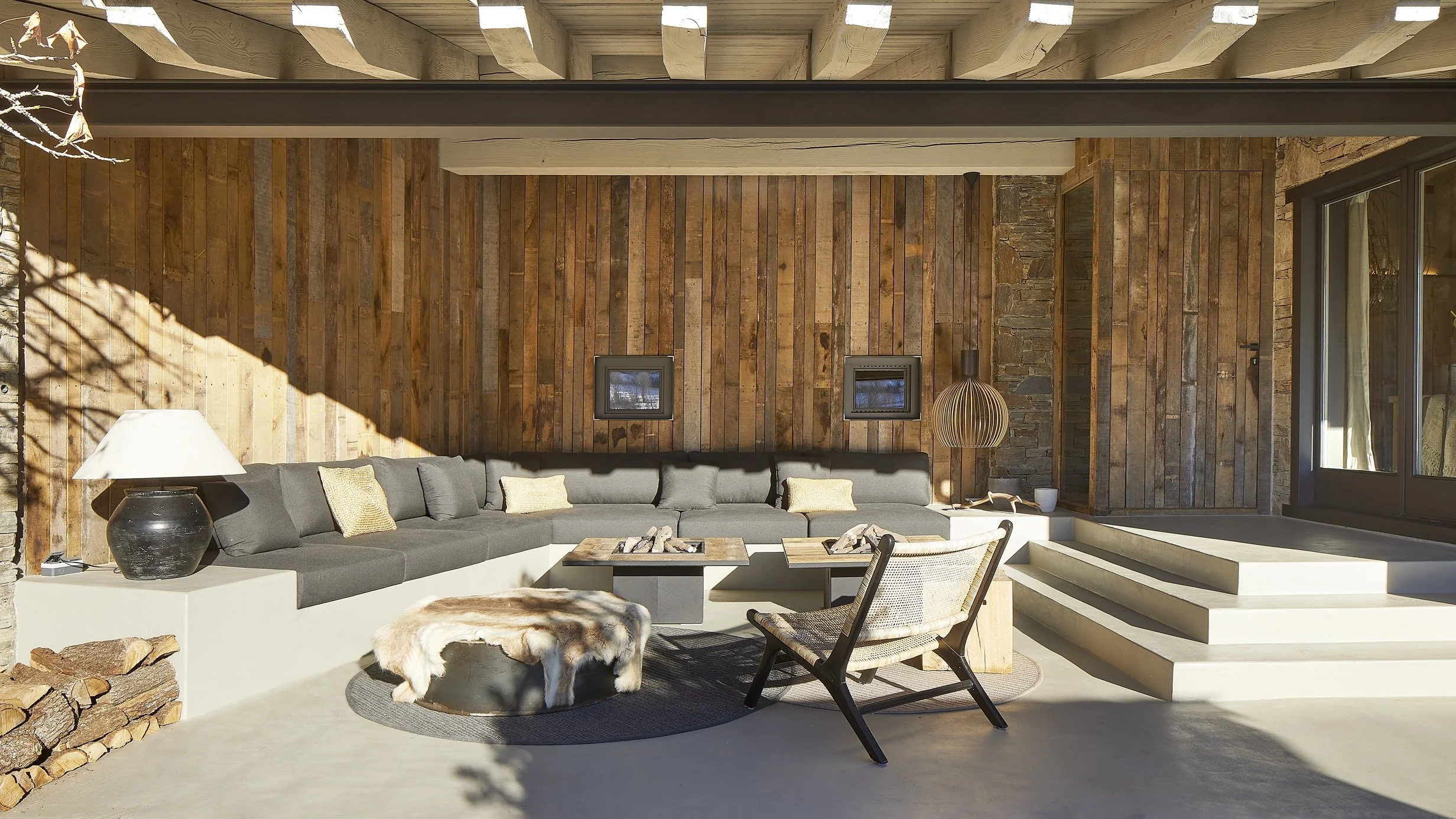 Salón de una vivienda unifamiliar reformada en Urús con hogar hundido, sofás grises y paredes de madera recuperada