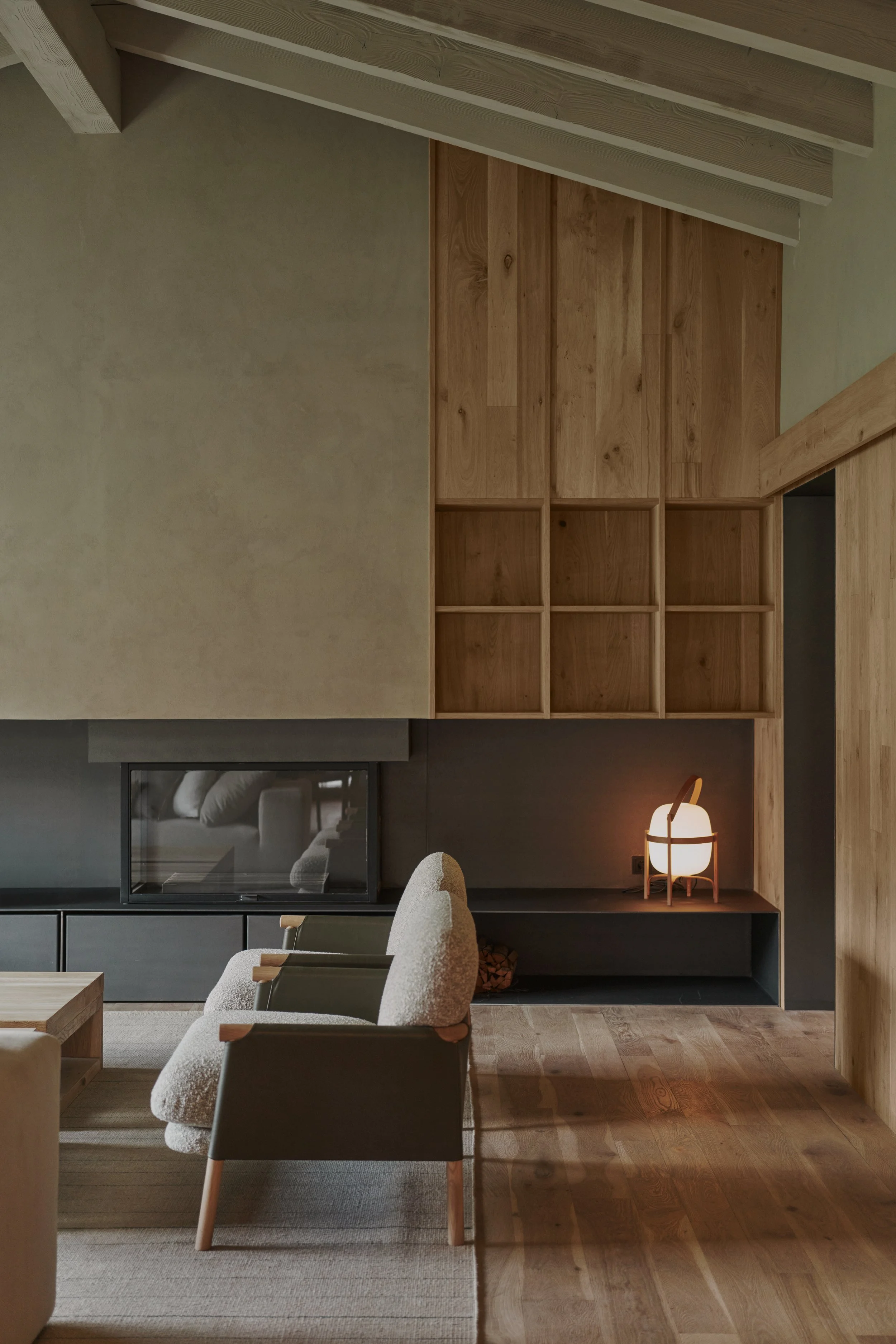 Salón con pared y estantería de madera, chimenea integrada, butaca de borreguito y lámpara portátil encendida
