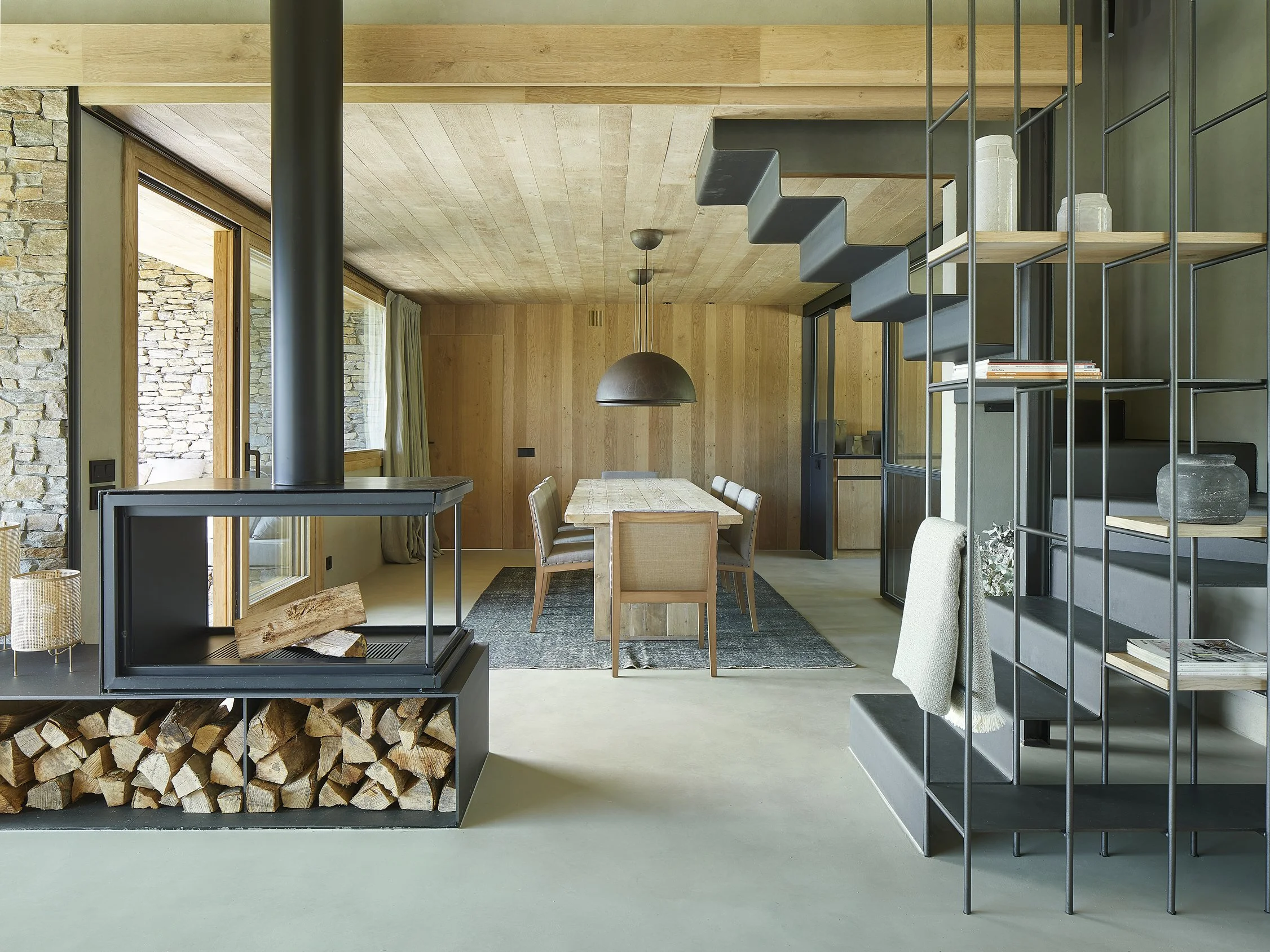 Salón con chimenea central suspendida, leñero y escalera de vidrio