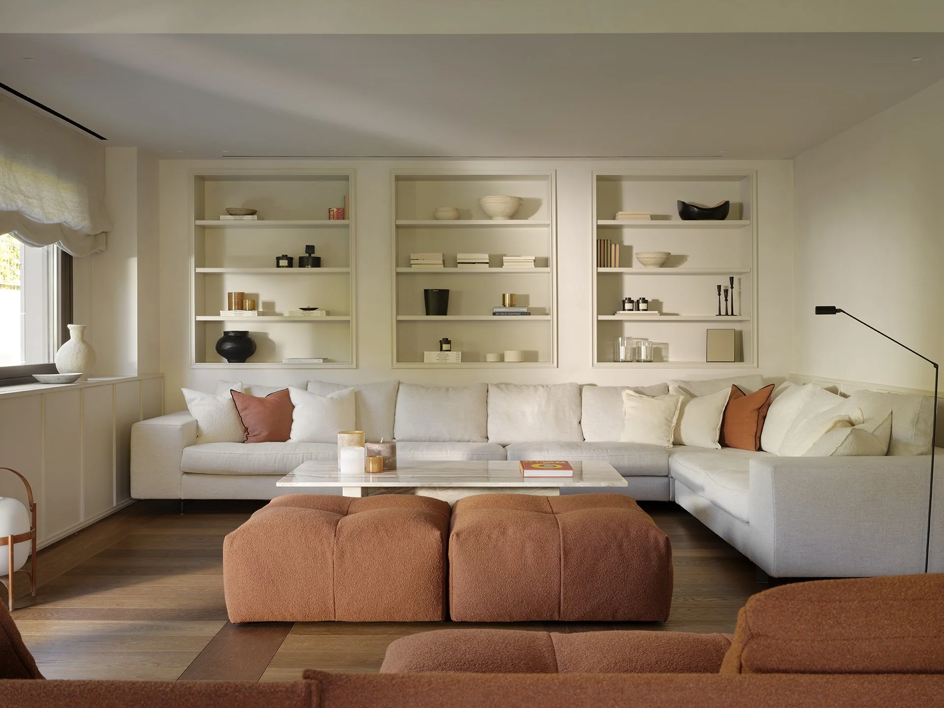 Salón con sofá blanco, pufs en tono terracota y estantería empotrada blanca con objetos decorativos