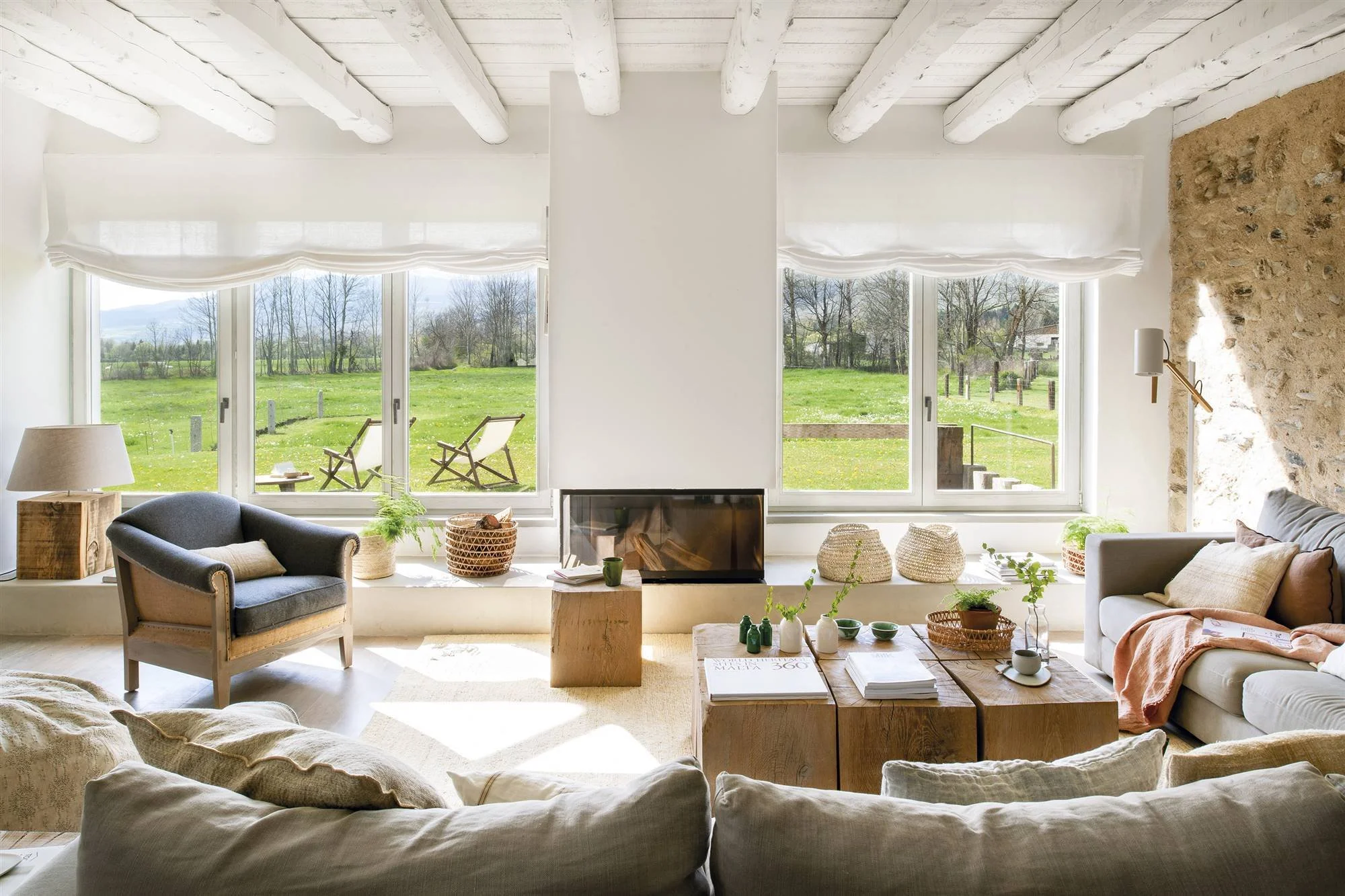 Salón con sofás en torno a una chimenea de vidrio y ventanales con vistas al jardín