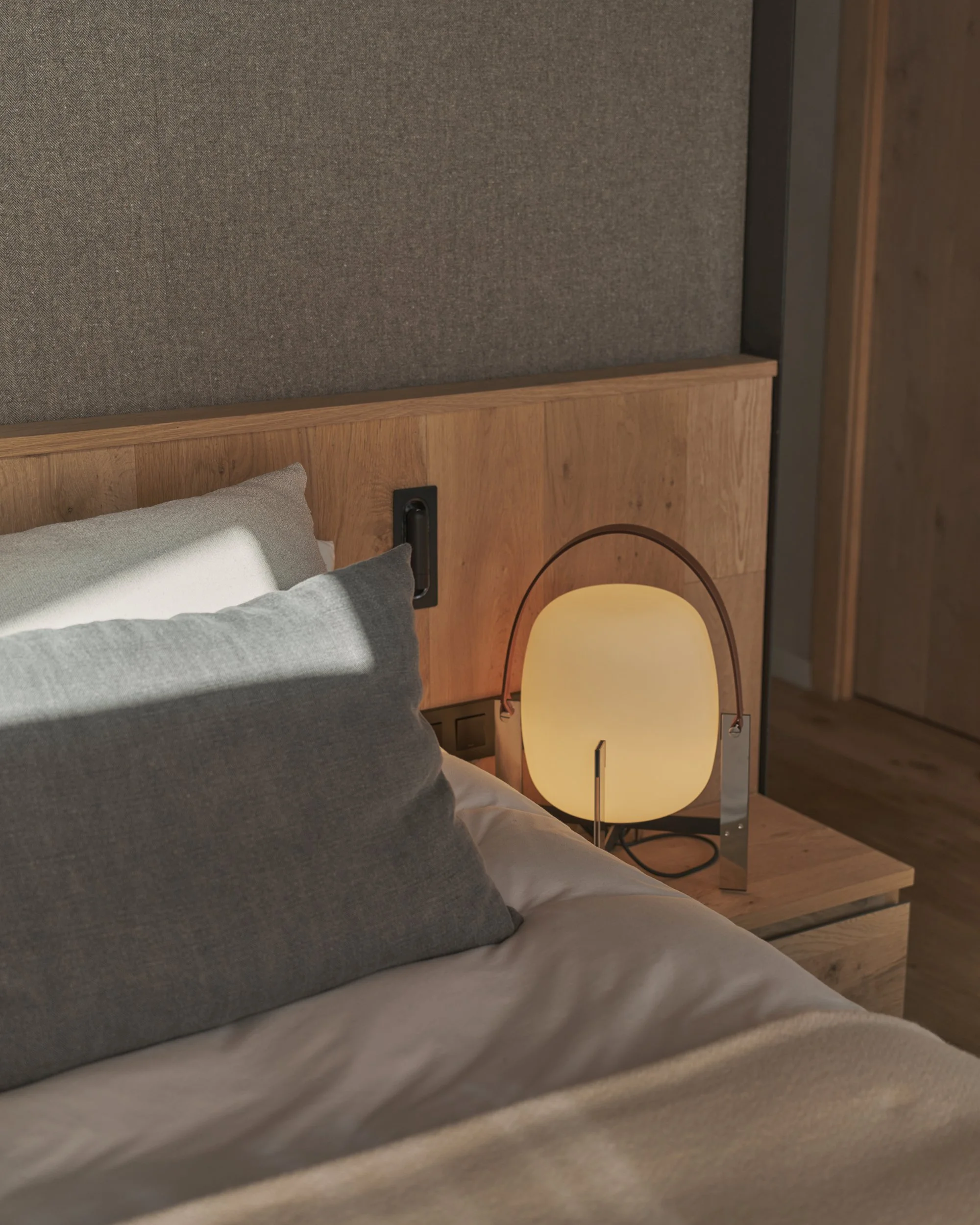 Dormitorio con cabecero de madera, ropa de cama en tonos gris topo y lámpara de mesa redonda