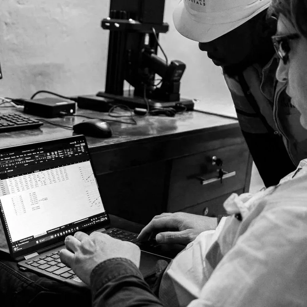 Two men working in Uganda, Africa with a laptop displaying data spreadsheets, with portable XRF unit (pXRF) in background.