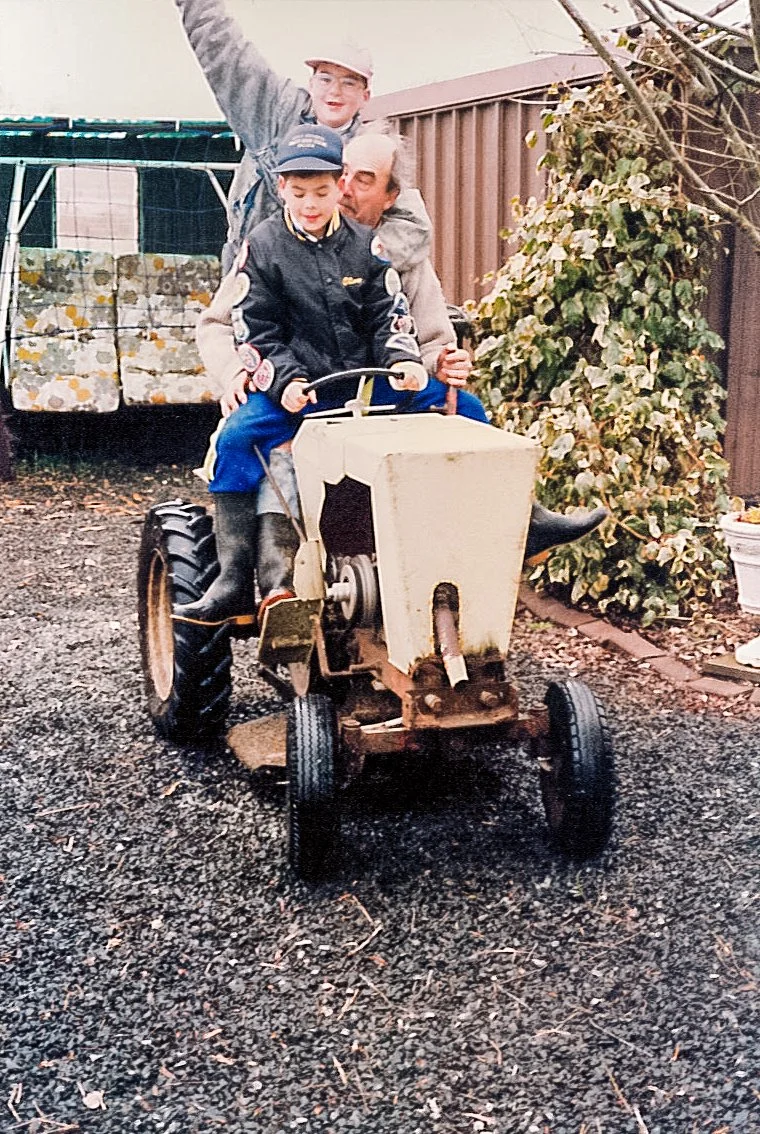 Three people riding a small tractor in a backyard setting.