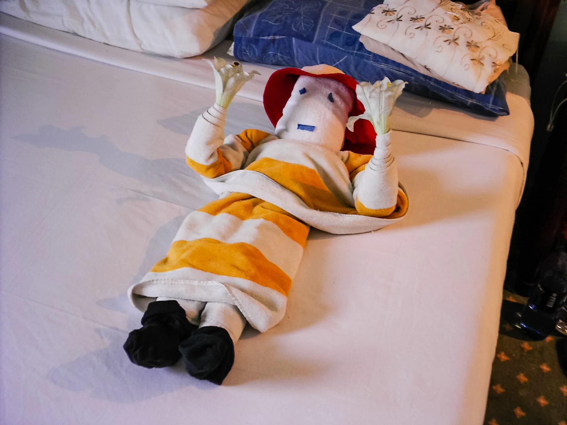 A towel arranged to resemble a figure wearing a hat, laid on a bed.