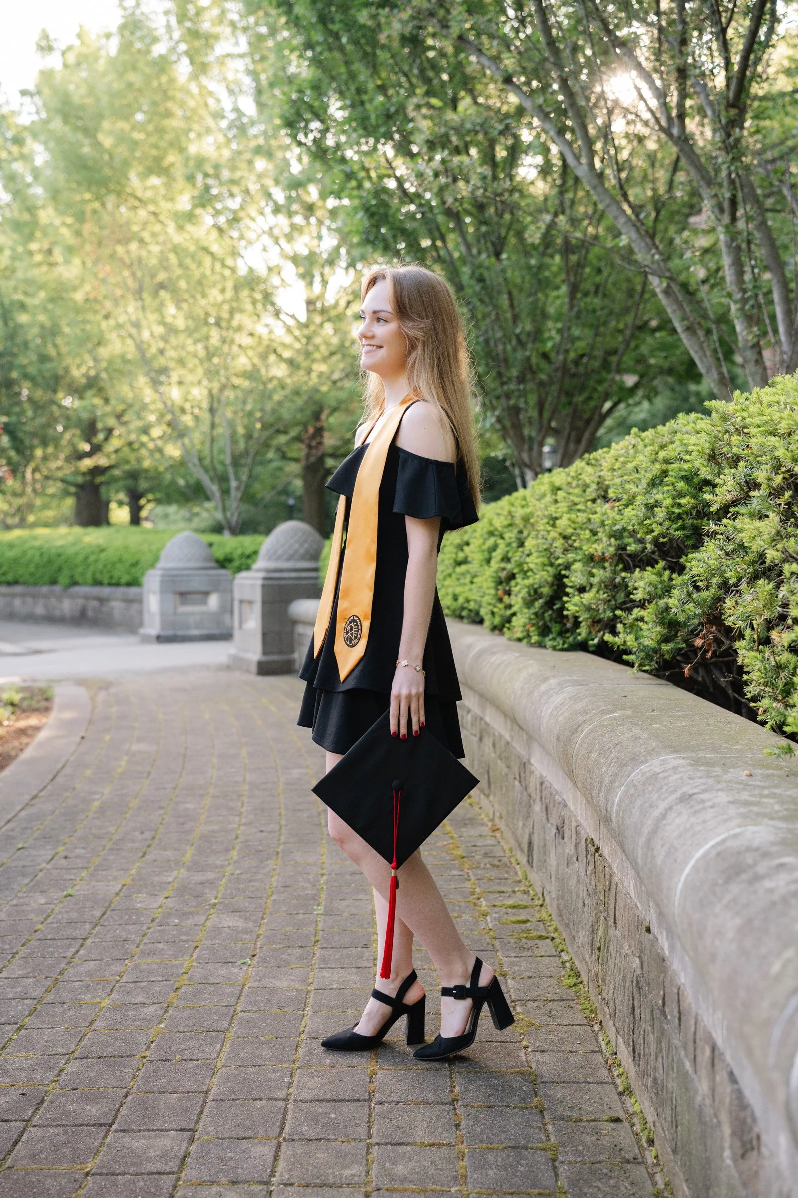 Purdue Graduate wearing a black dress with her gold Purdue stoles around her neck and holding her cap.