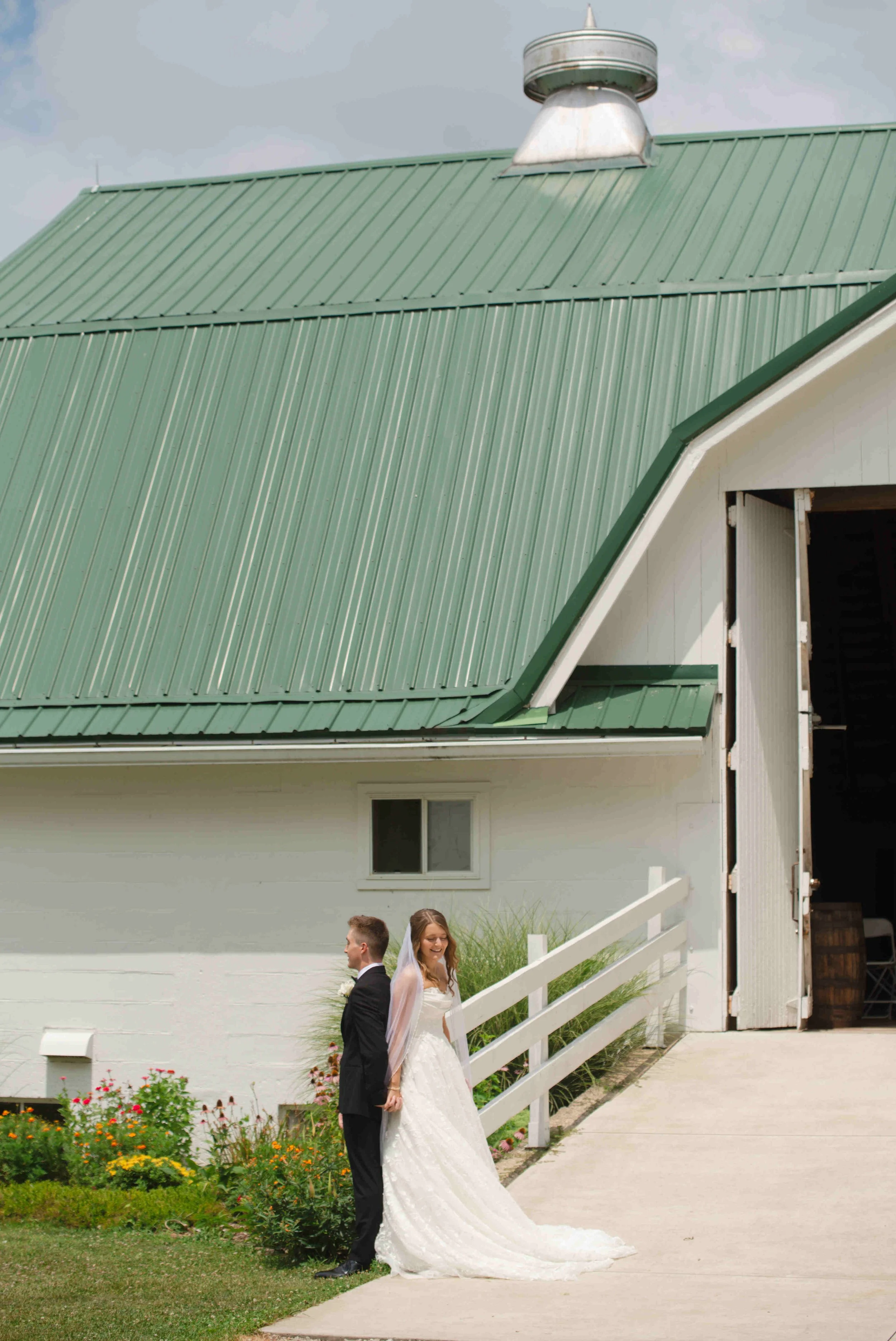 Bride and groom standing back to back at white fence in front of the barn at For-Lou Farms for a "first touch" time of prayer before their wedding ceremony.  Photo by Heather Corbin Photography