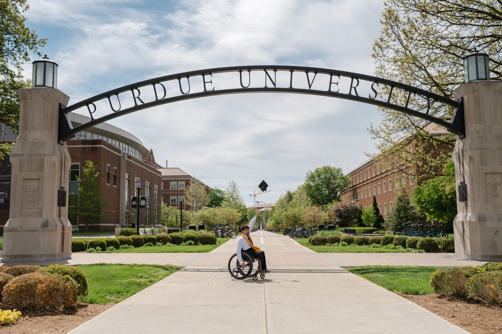 Purdue graduate in a wheelchair under the Purdue Arch throwing cap up in the air photo by Heather Corbin Photography