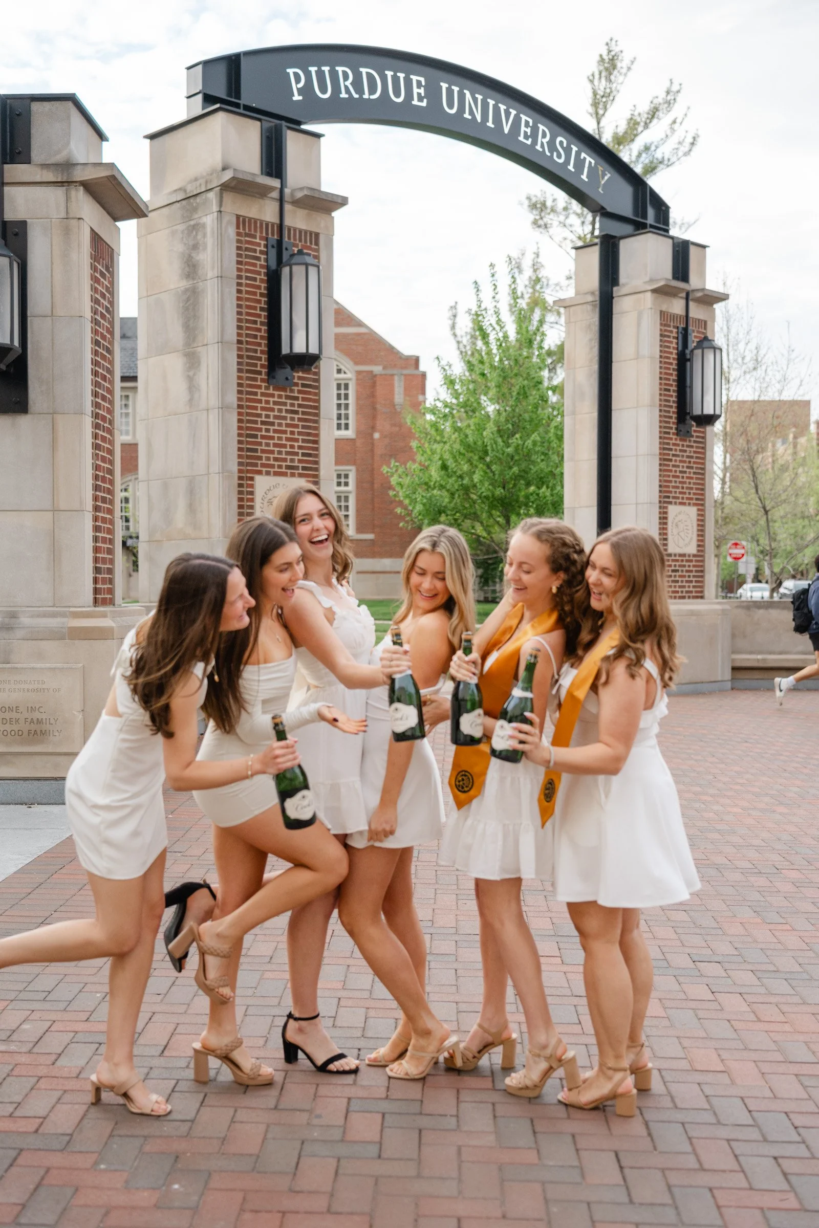 Group of Purdue grads in white dresses ready to spray their celebratory Champagne bottles