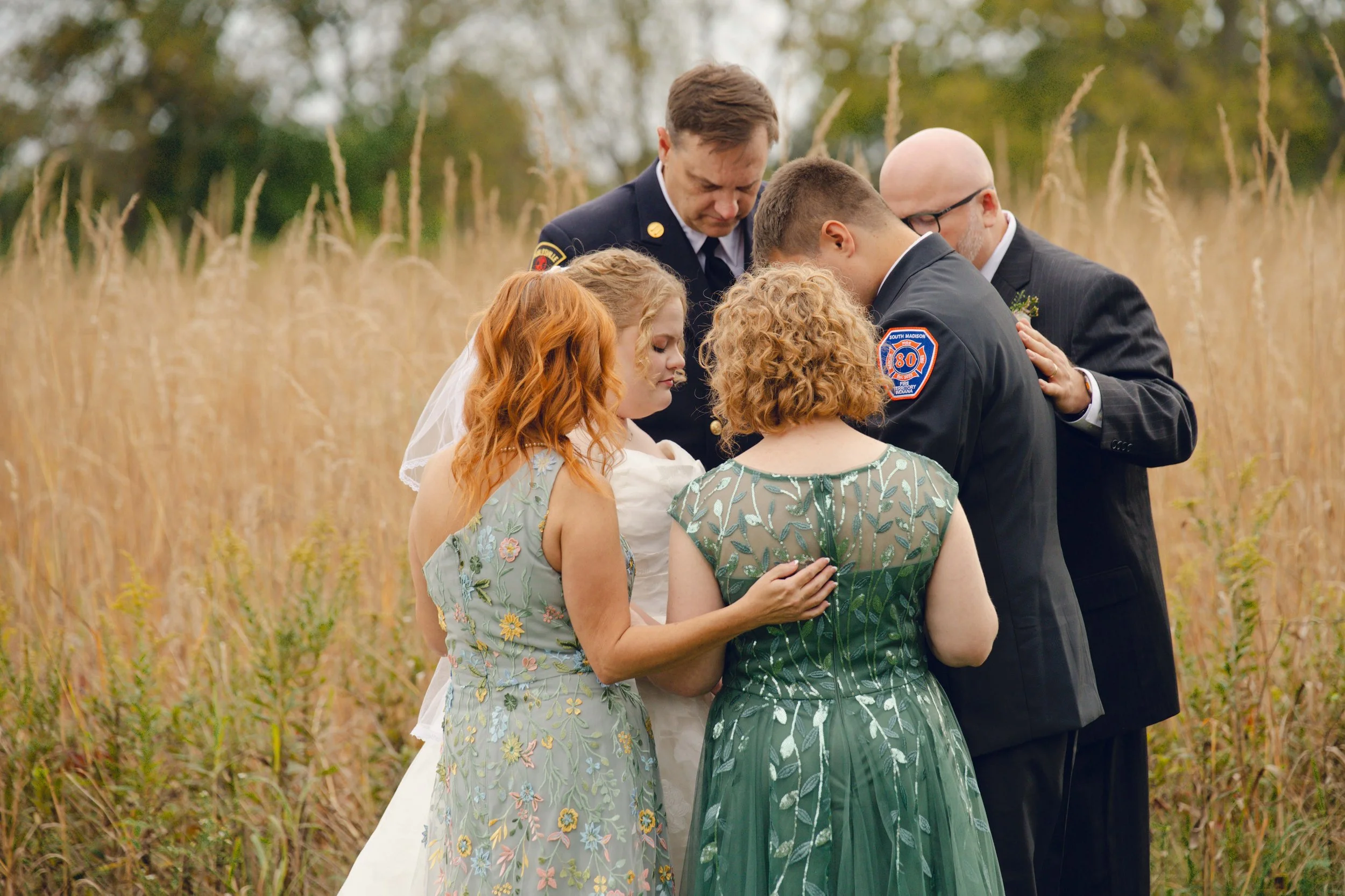 Parents of bride and groom laying hands on the couple and praying blessings over them during the wedding ceremony held at prophetstown state park, Indiana.