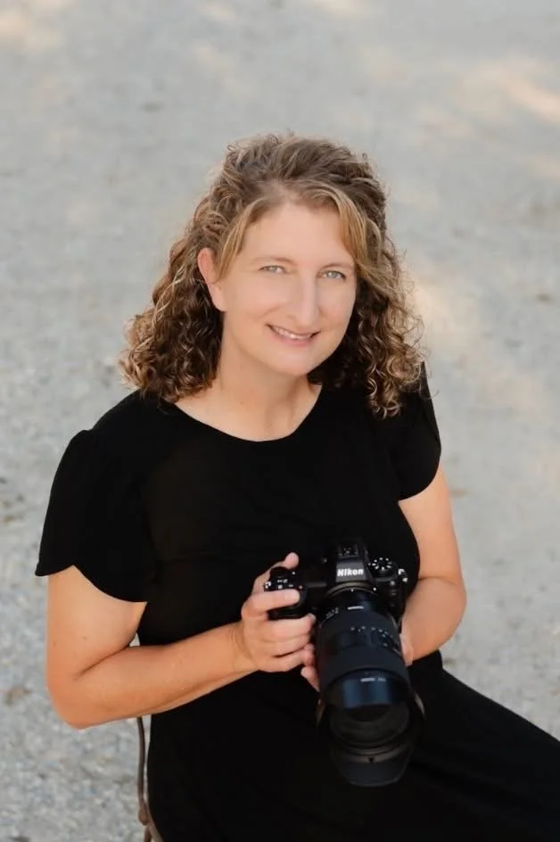 Heather Corbin in black dress holding nikon camera headshot.  Heather Corbin Photography