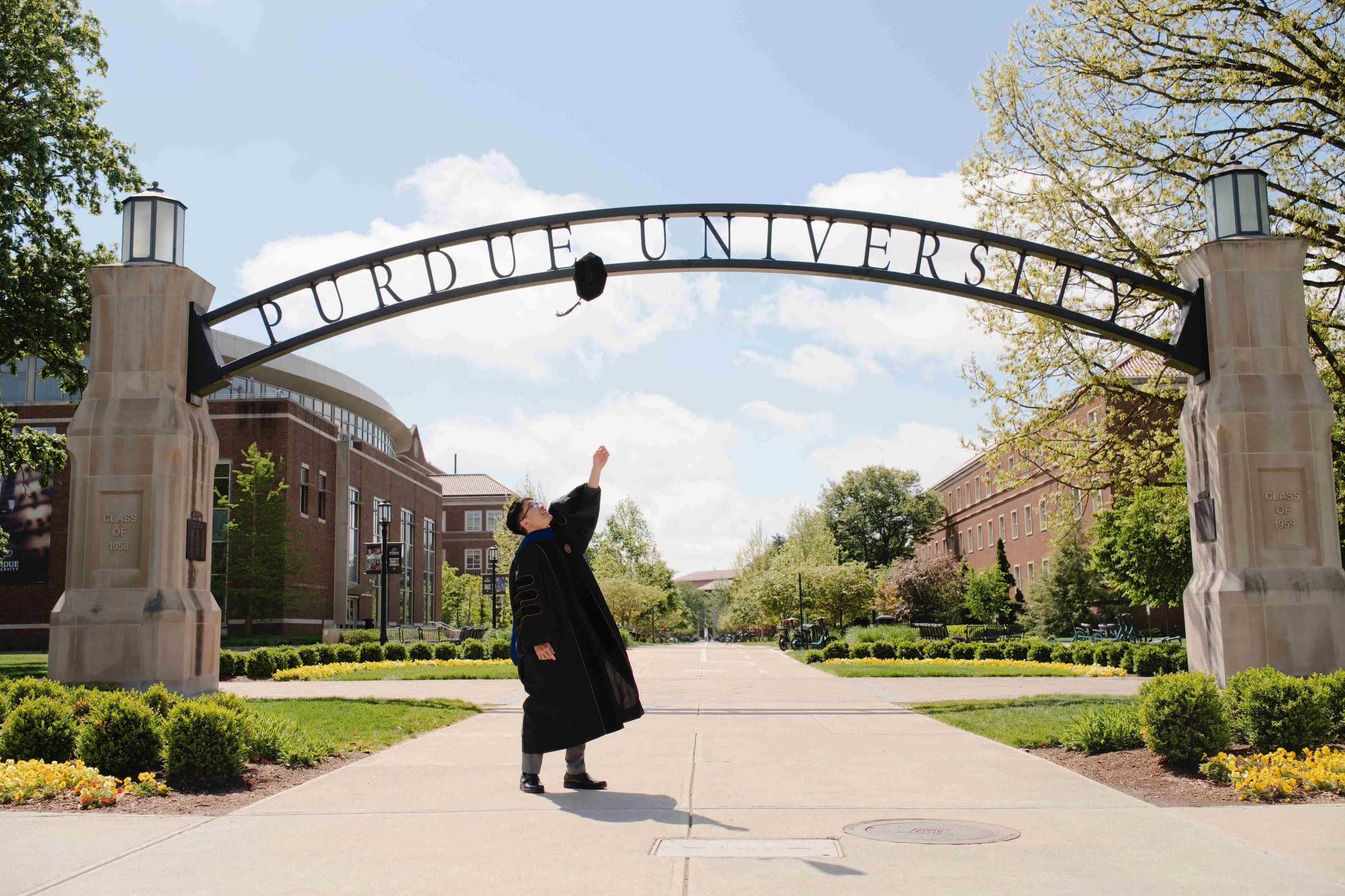 Purdue PhD graduate tossing cap in front of the gateway arch at Purdue University during Graduation photo session by Heather Corbin Photography