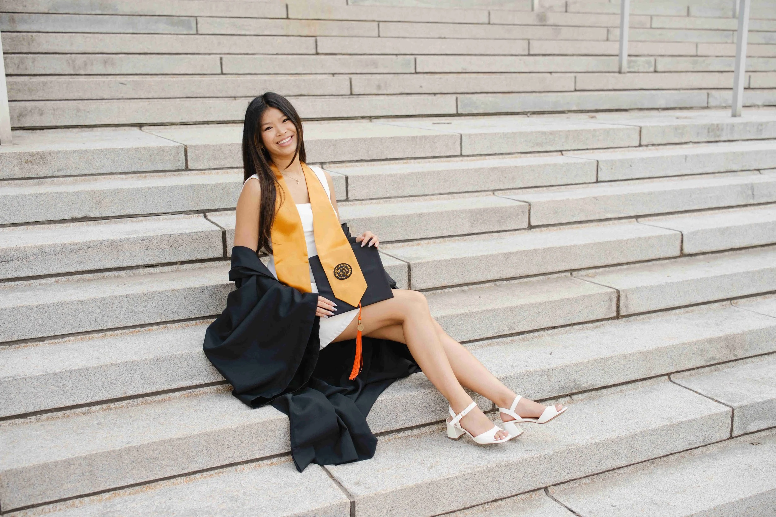 Purdue graduate sitting on hovde steps holding cap during photo session by heather corbin photography