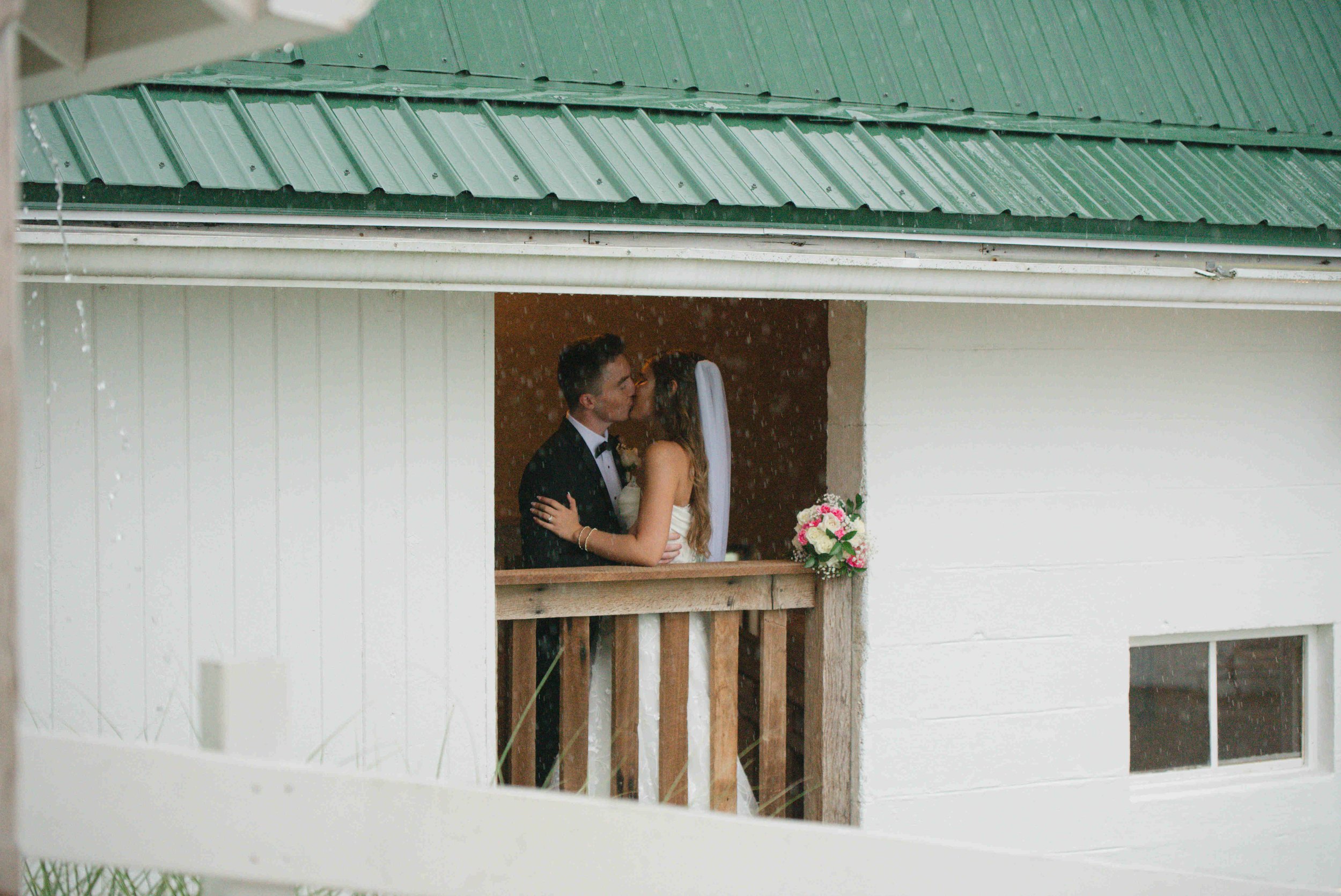 Bride and groom kissing at window while it rains outside on their wedding day at For-Lou Farms.
