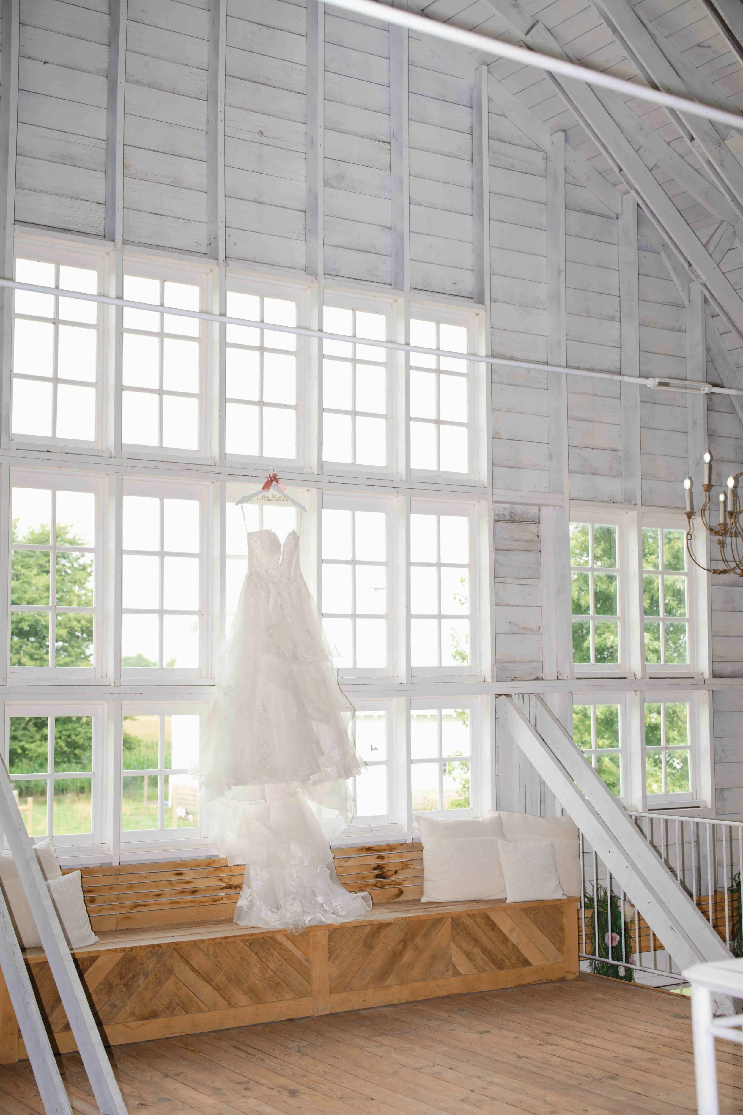Wedding Dress hanging on the very large windows of the loft at blossom barn, Mulberry Indiana.  Photo by Heather Corbin Photography.