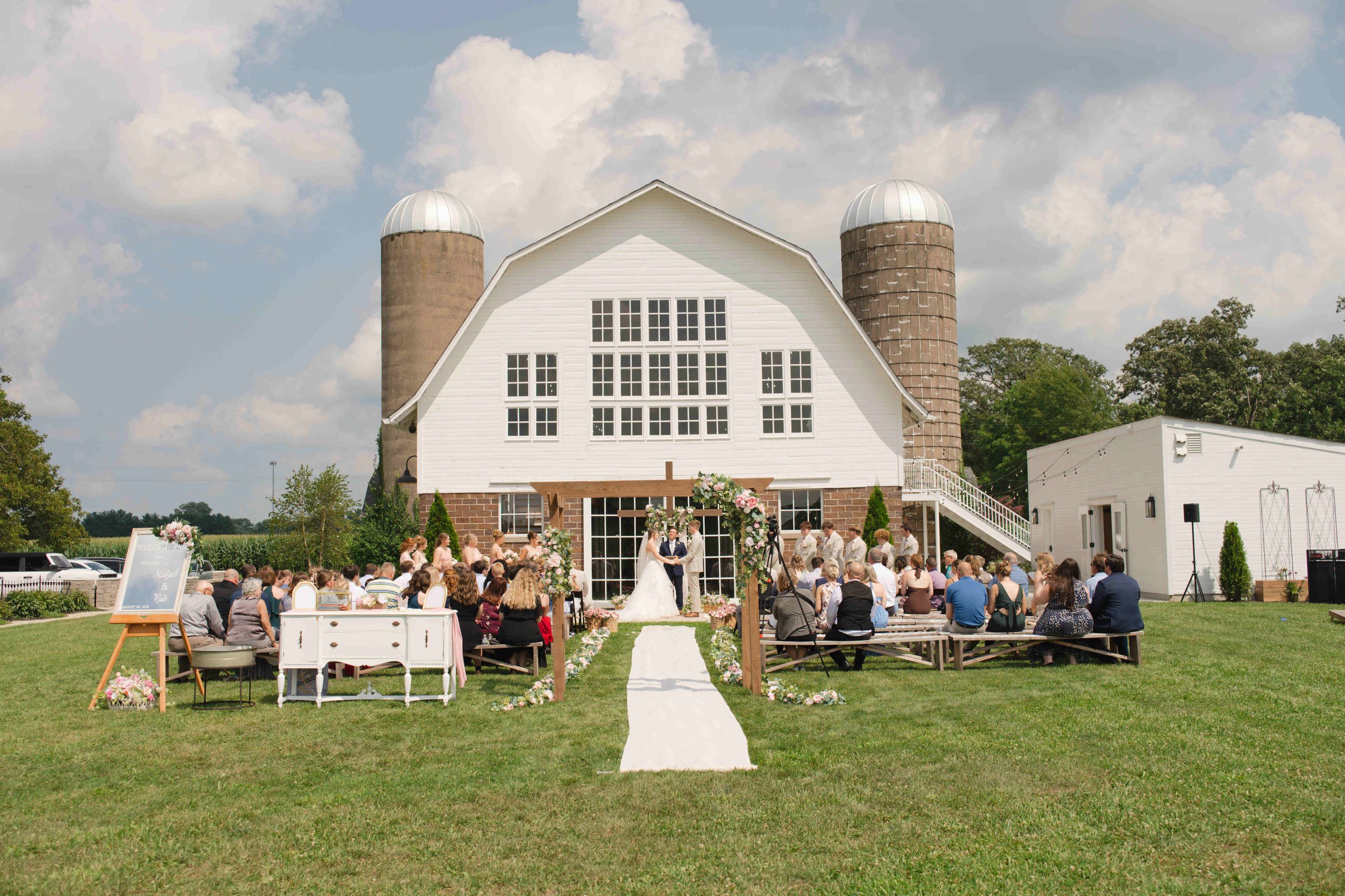 Bride and groom standing in front of a cross with the barn at Blossom Barn, Mulberry Indiana, serving as the beautiful backdrop