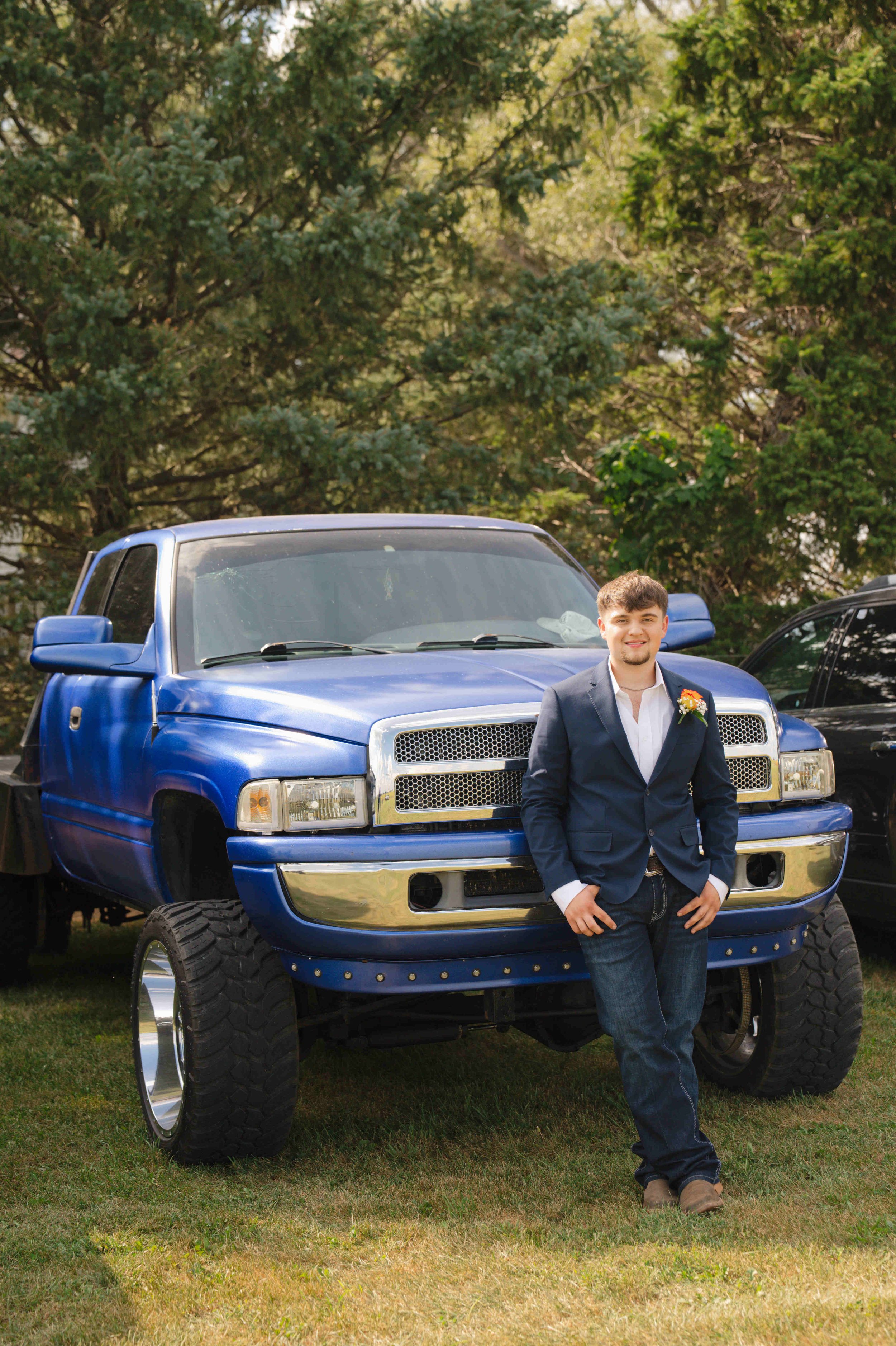 Groom wearing jeans, boots, and a blue jacket standing in front of his 2001 Dodge 2500, 24 valve diesel.  Wedding at Governors Pavilion, Wolcott In