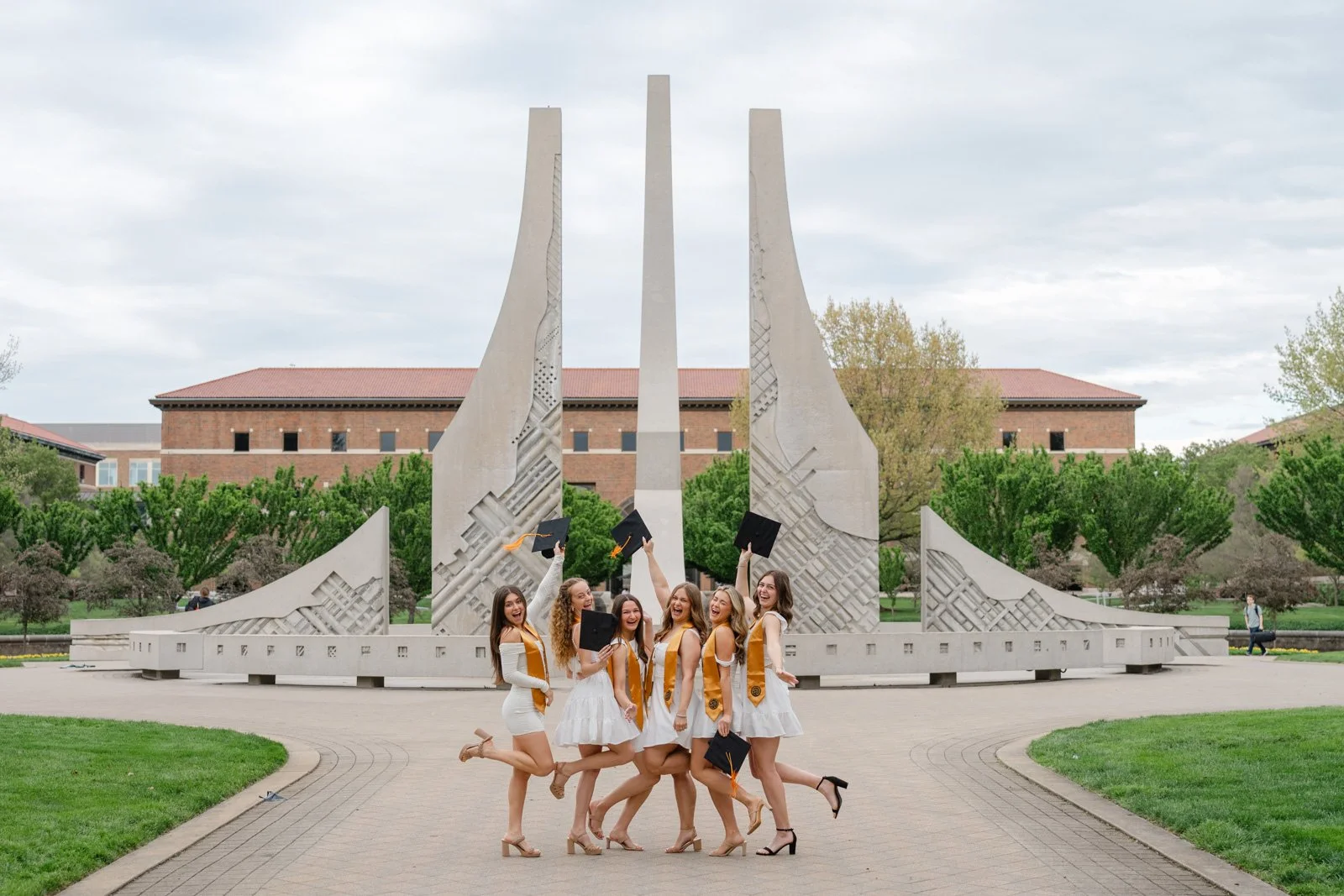 Friend group of Purdue Nursing Students cheering with graduation caps raised. Engineering fountain in the background.  Photo by Heather Corbin Photography